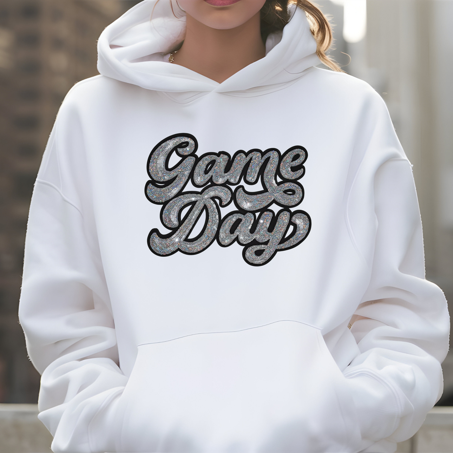 White hoodie with 'Game Day' text worn by a person, blurred background
