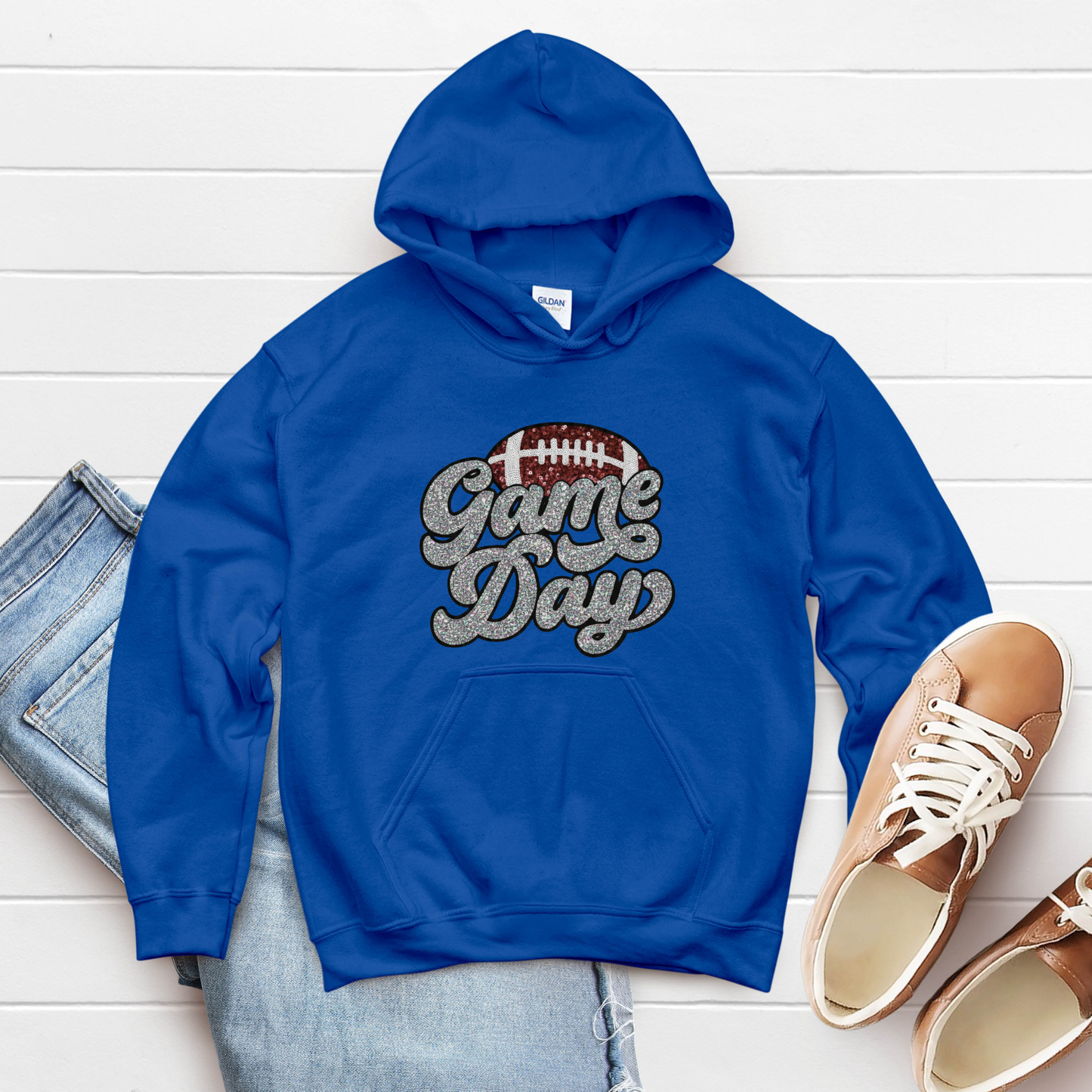 Blue hoodie with 'Game Day' text, jeans, and shoes on a white wooden surface