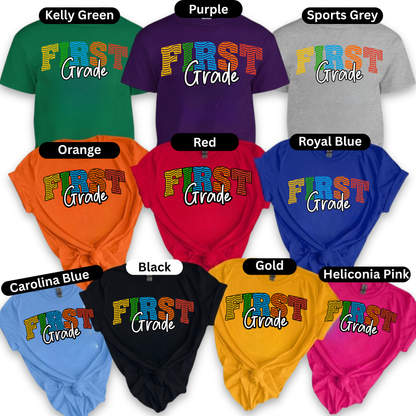 A collage showing multiple color options of a short-sleeve t-shirt with a colorful 'FIRST Grade' graphic on the front. The shirts are shown in green, purple, grey, orange, red, royal blue, Carolina blue, black, gold, and heliconia pink, each labeled with its color name at the top.