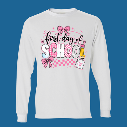 A white long-sleeve t-shirt with a 'first day of SCHOOL' graphic on the chest, displayed against a solid blue background.