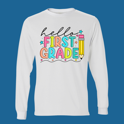 A white long-sleeve t-shirt with a colorful 'Hello First Grade' graphic on the chest, displayed against a solid blue background.