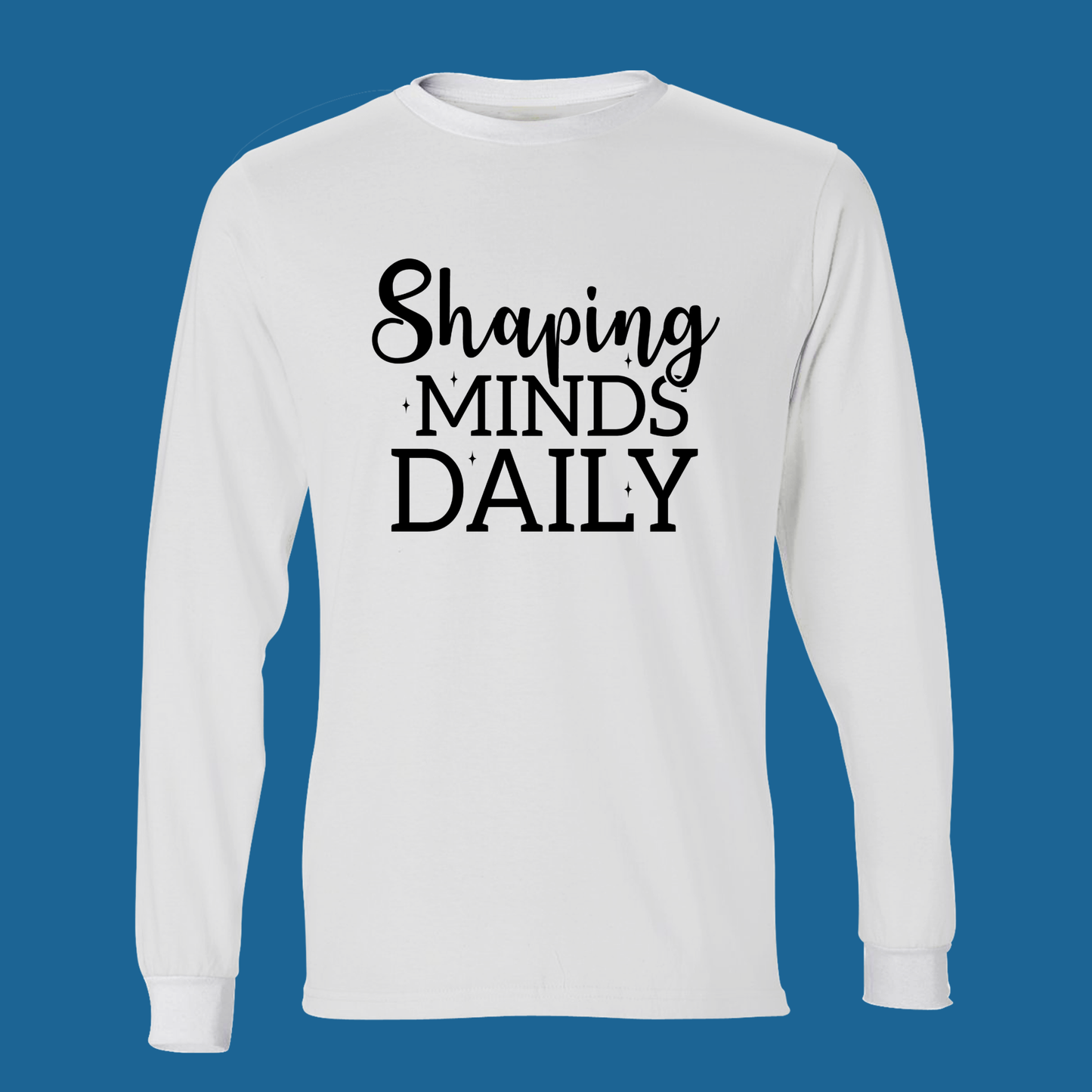 A white long-sleeve t-shirt with the text 'Shaping MINDS DAILY' printed in black on the chest, displayed against a solid blue background.