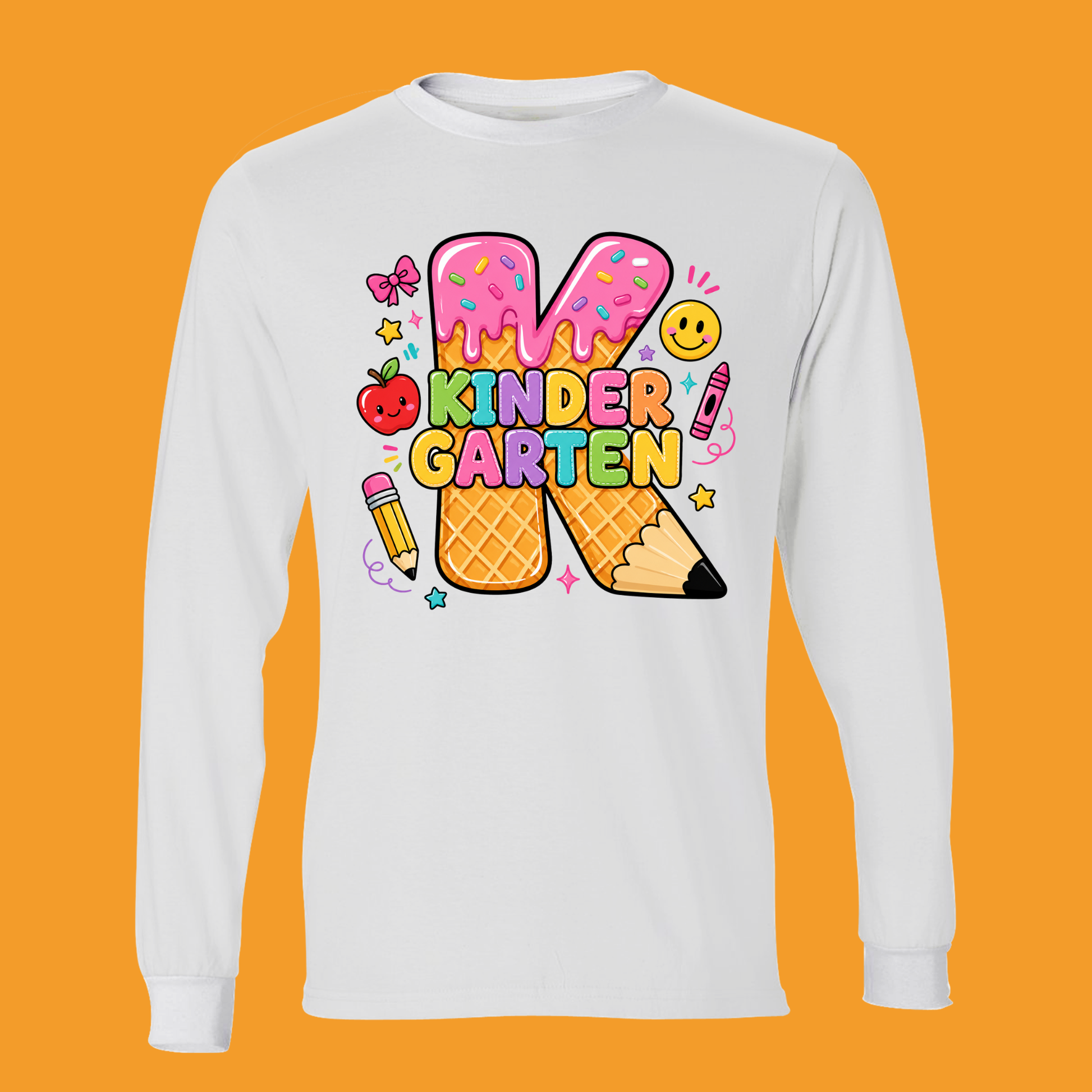 A white long-sleeve t-shirt with a colorful graphic on the front. The graphic features a large letter 'K' styled as a waffle cone with pink frosting, surrounded by cute school-themed illustrations like a smiling apple, bow tie, smiley face, and crayons, with the text 'KINDER GARTEN' written in a playful multicolor font.