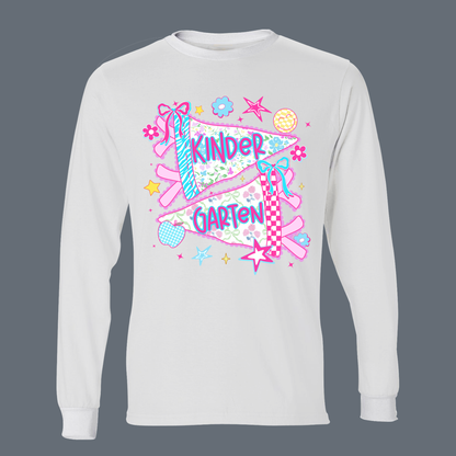 A white long-sleeve t-shirt with a colorful graphic on the front featuring a kite and the words 'KINDER GARTEN' in purple, surrounded by pink, blue, and yellow decorative elements, shown against a solid dark gray background.