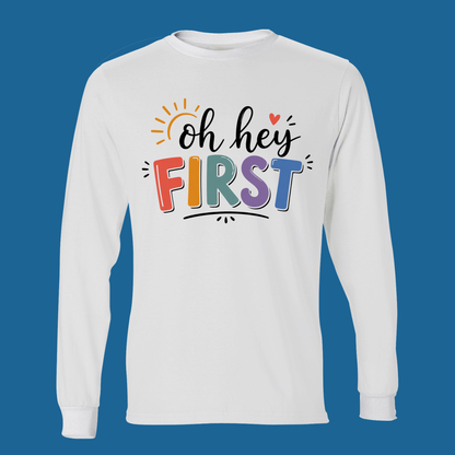 A white long-sleeve t-shirt with a colorful graphic on the chest reading 'Kinder Garten' in a floral pattern, decorated with small gardening icons and a pink ribbon bow underneath, set against a solid blue background.
