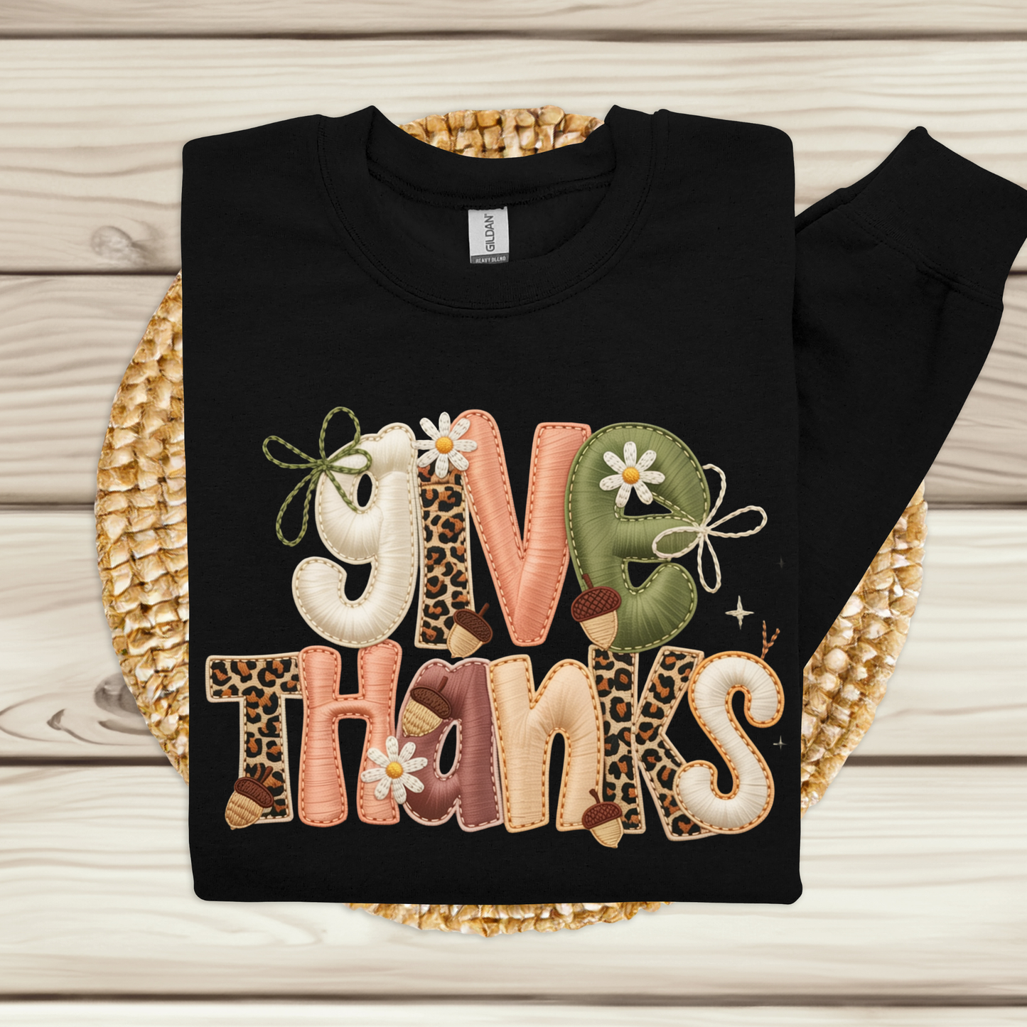 Black sweatshirt with 'Give Thanks' text in colorful letters on a woven mat.