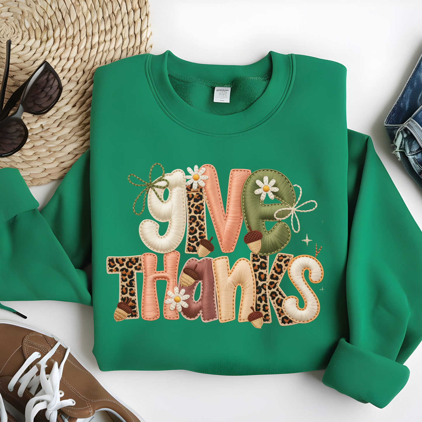Green sweatshirt with 'Give Thanks' text on a white surface with accessories.