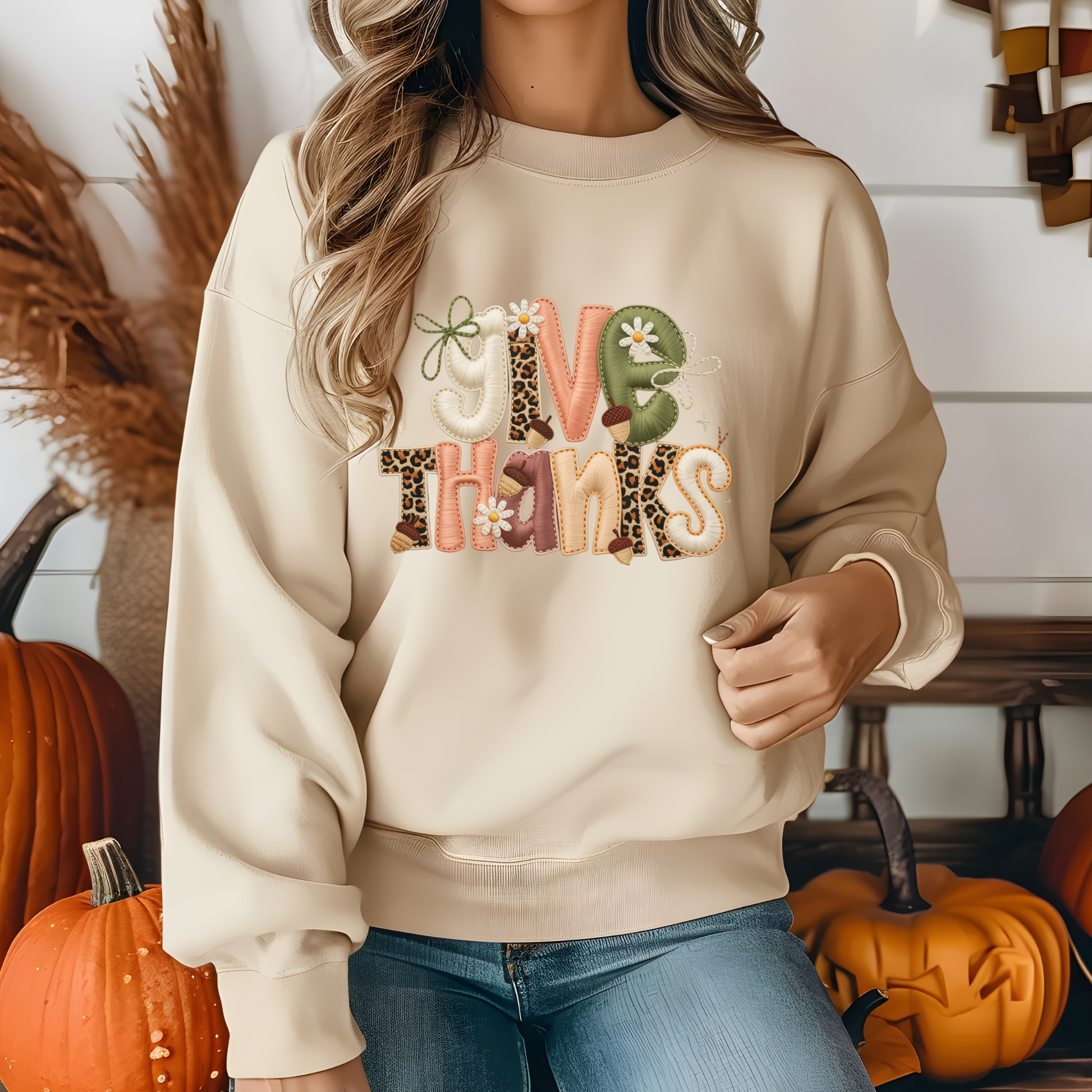 Person wearing a beige sweatshirt with 'Give Thanks' text in colorful letters, surrounded by pumpkins.