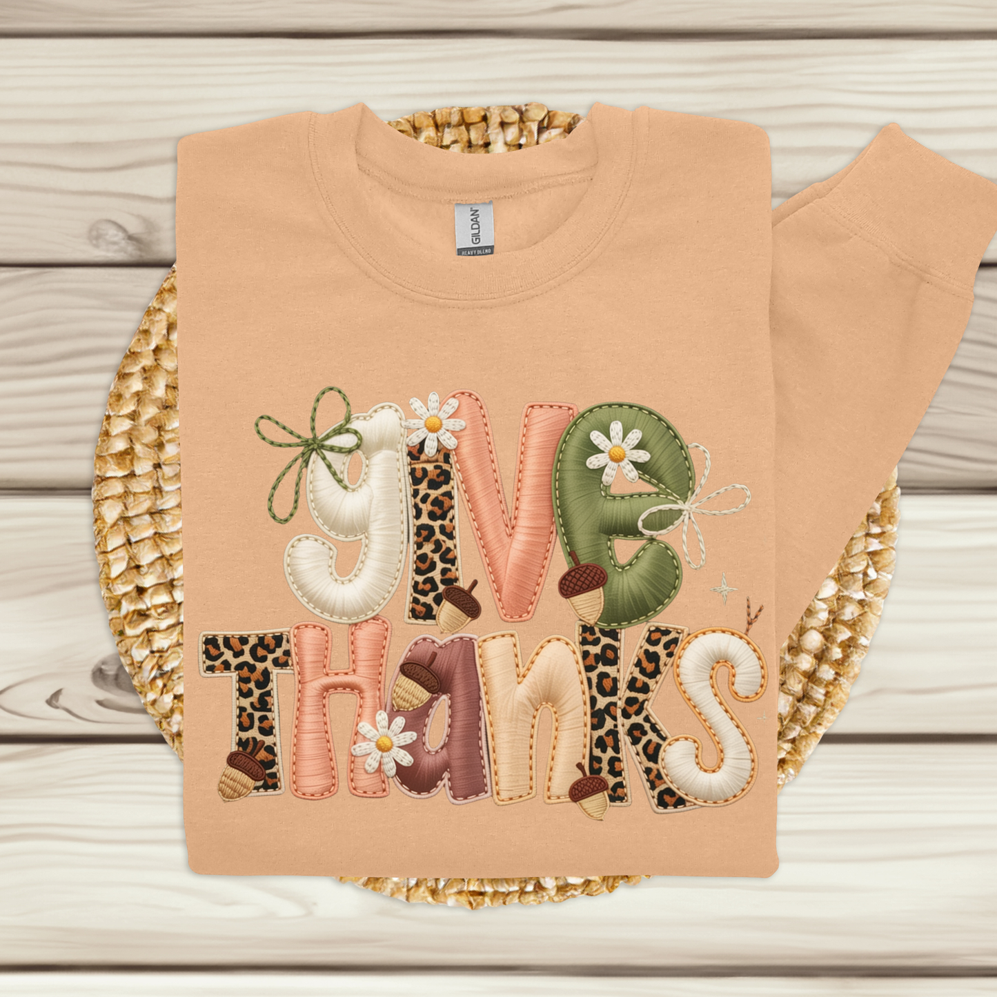 Beige sweatshirt with decorative text and patterns on a wooden surface