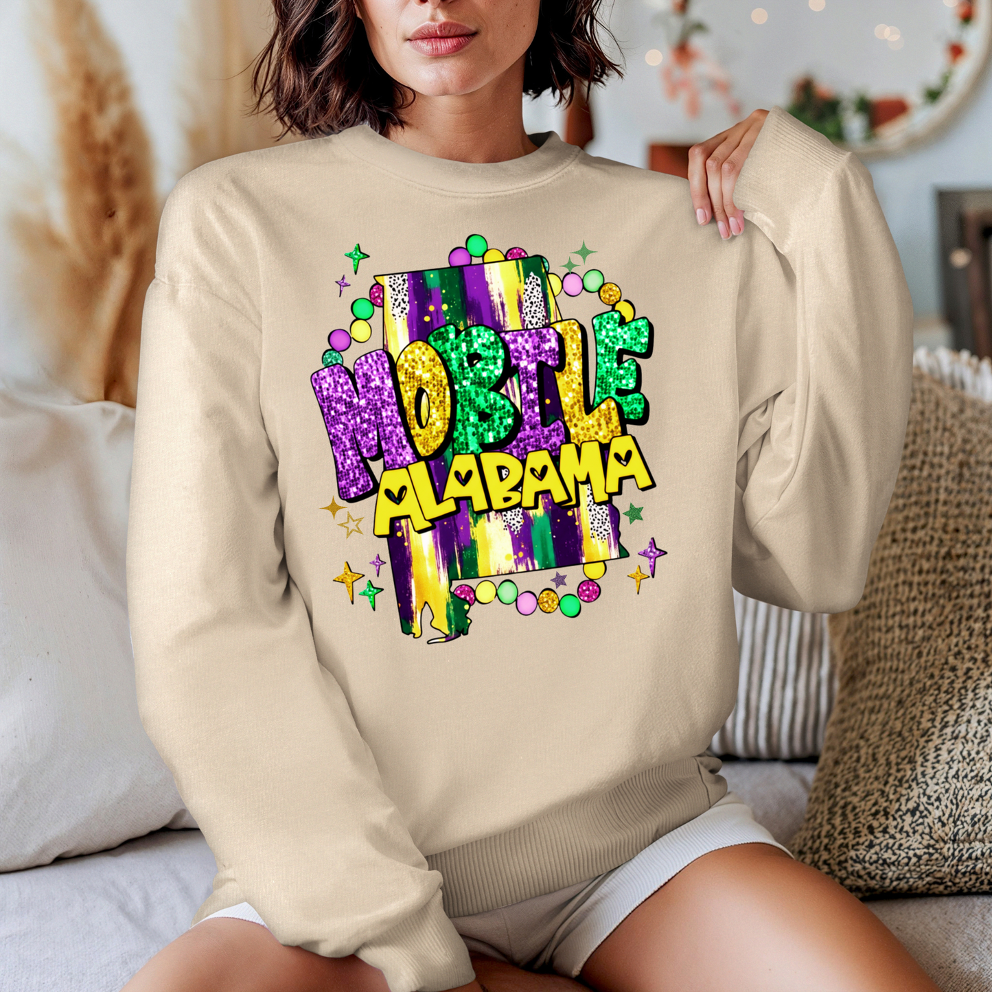 Person wearing a beige sweatshirt with colorful 'Mobile, Alabama' design.