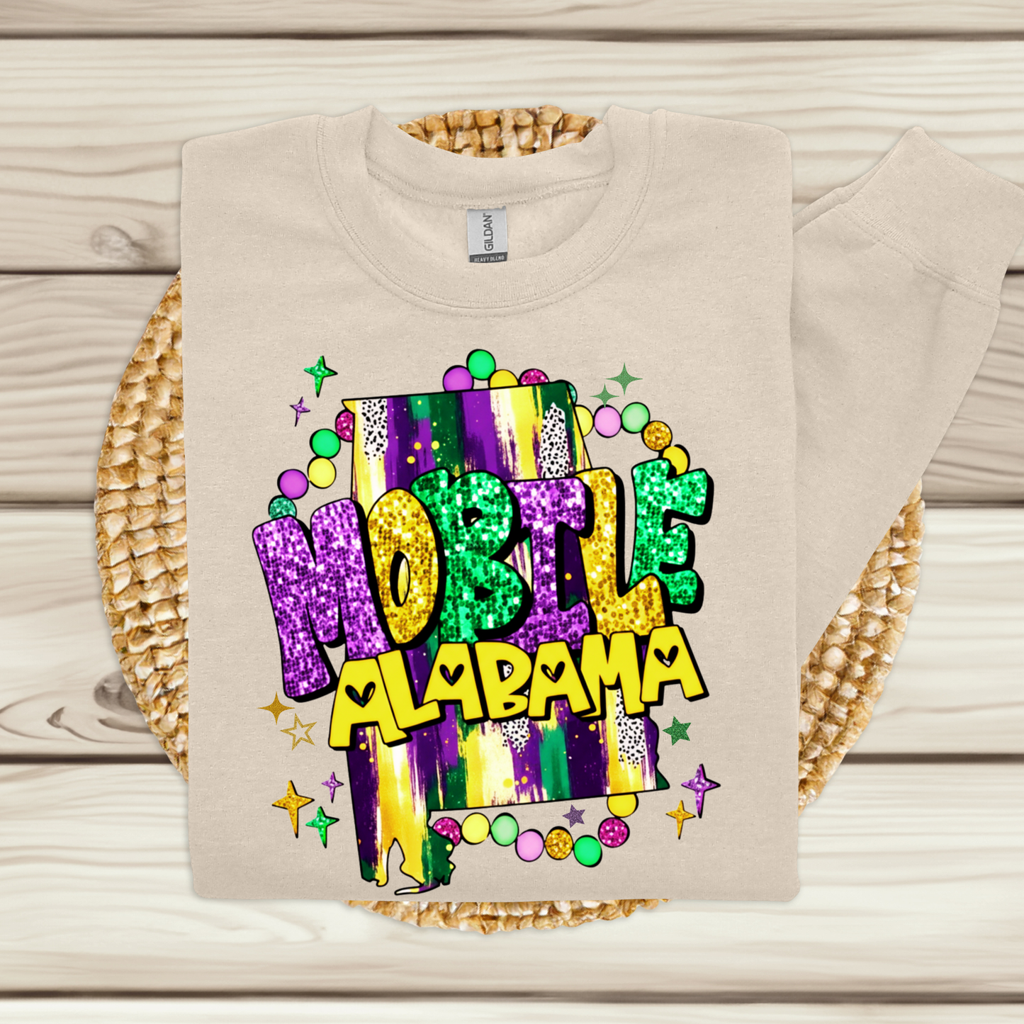Beige t-shirt with colorful 'Mobile, Alabama' design on a wooden surface