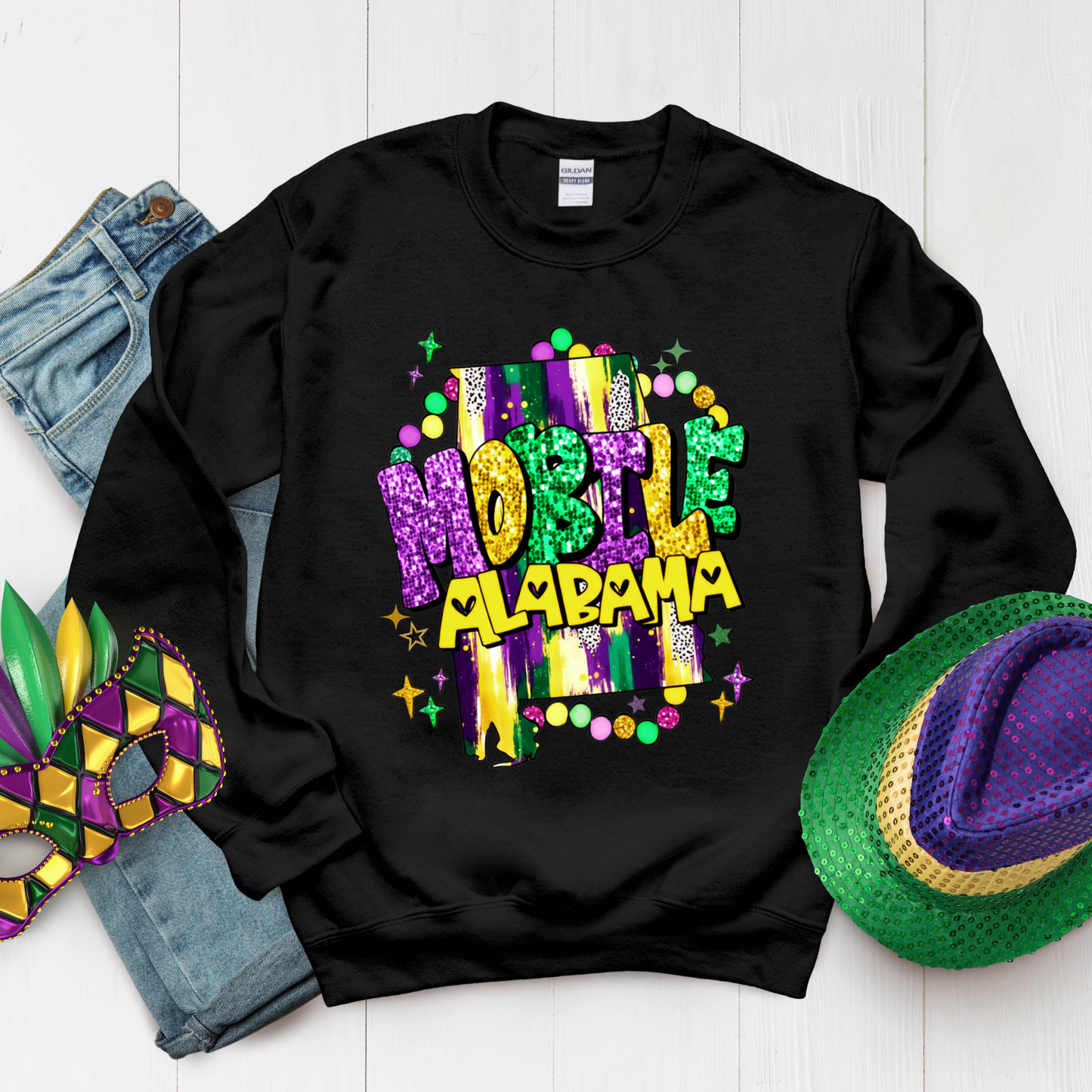 Black sweatshirt with colorful 'Mardi Gras Mobile Alabama' text, surrounded by Mardi Gras-themed accessories on a white background.