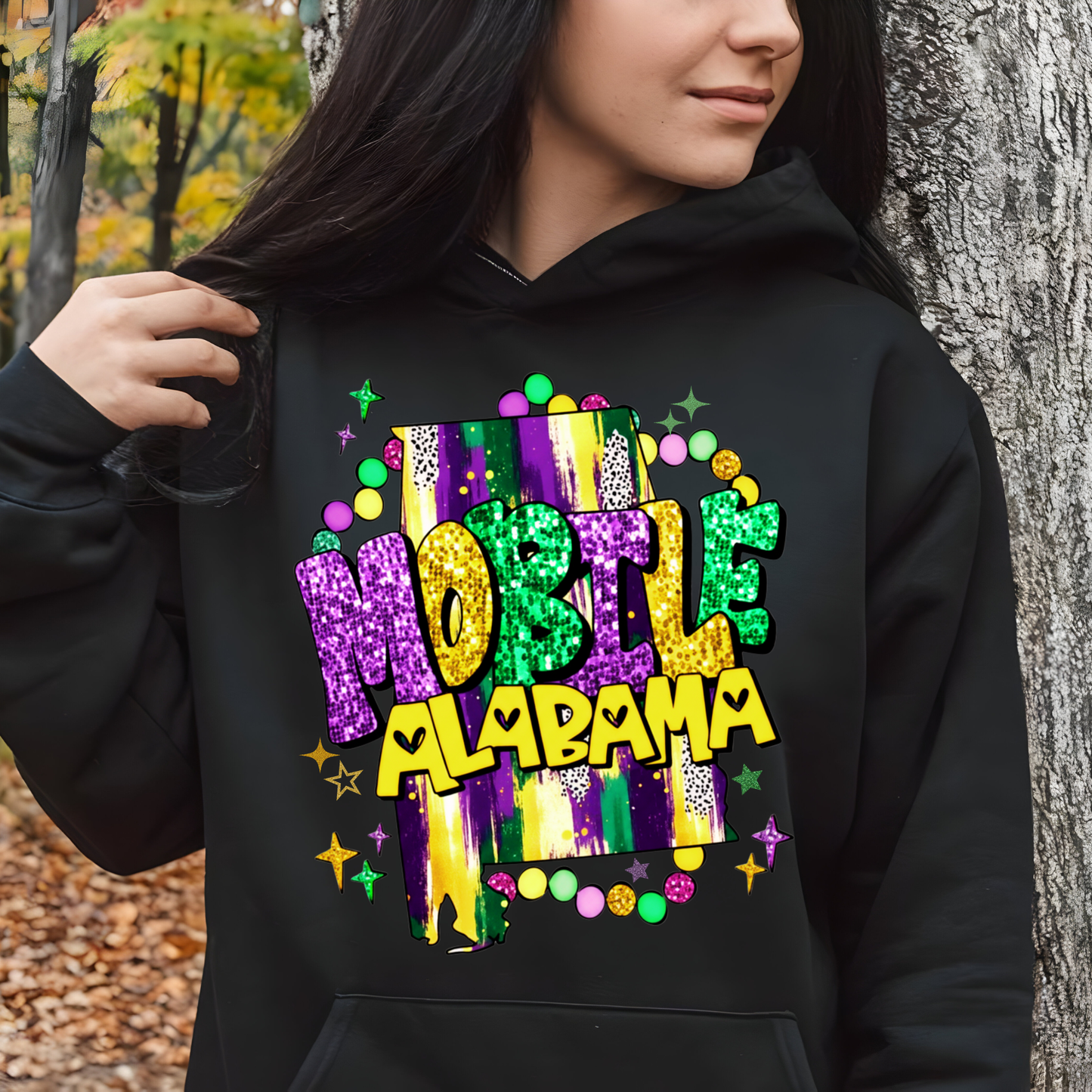 Person wearing a black hoodie with colorful 'Hobbe Alabama' text design outdoors.