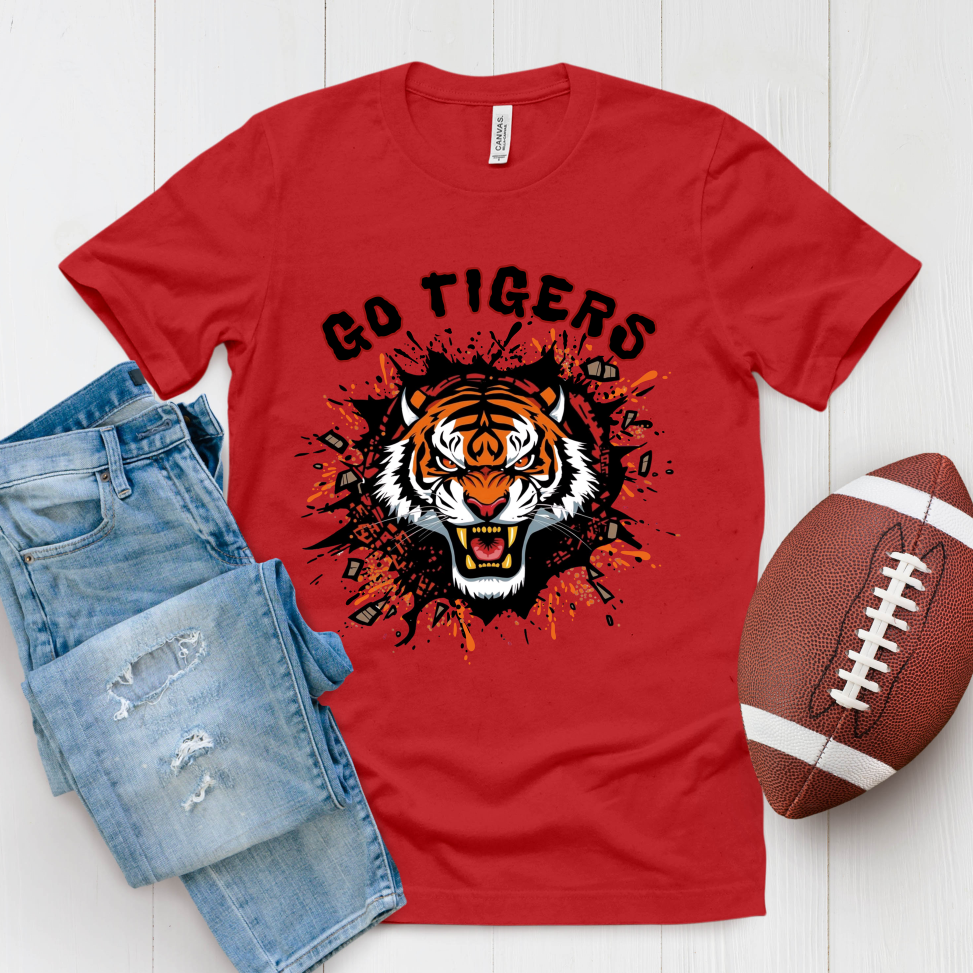 Red t-shirt with tiger graphic and 'Go Tigers' text, paired with jeans and a football on a white background. Go Tigers Bold Mascot Tee – Unleash Your School Spirit