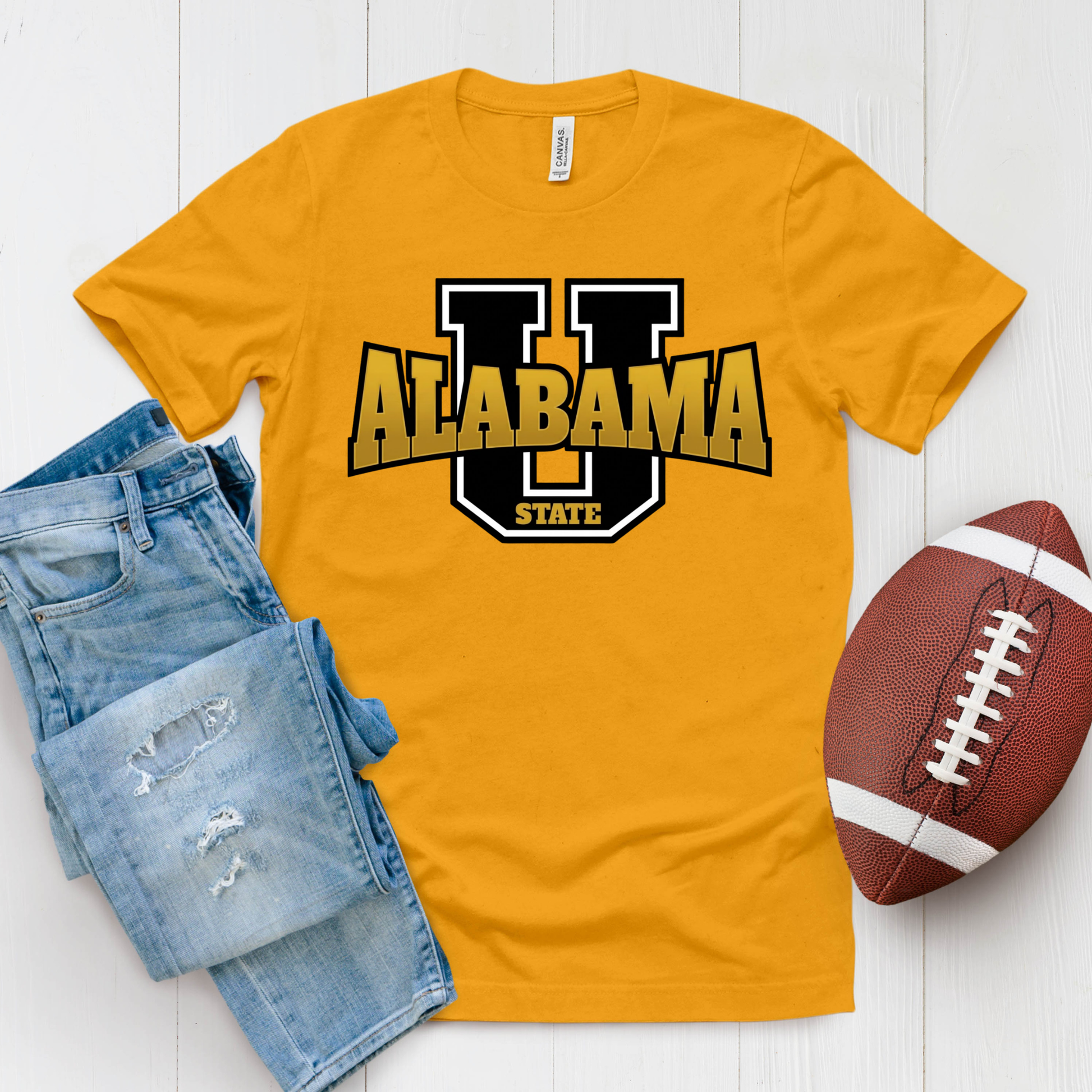 A gold crewneck t-shirt featuring a 'Hornets Nation' graphic with a hornet mascot, styled in a flat lay with blue jeans and a brown football on a white wood background.