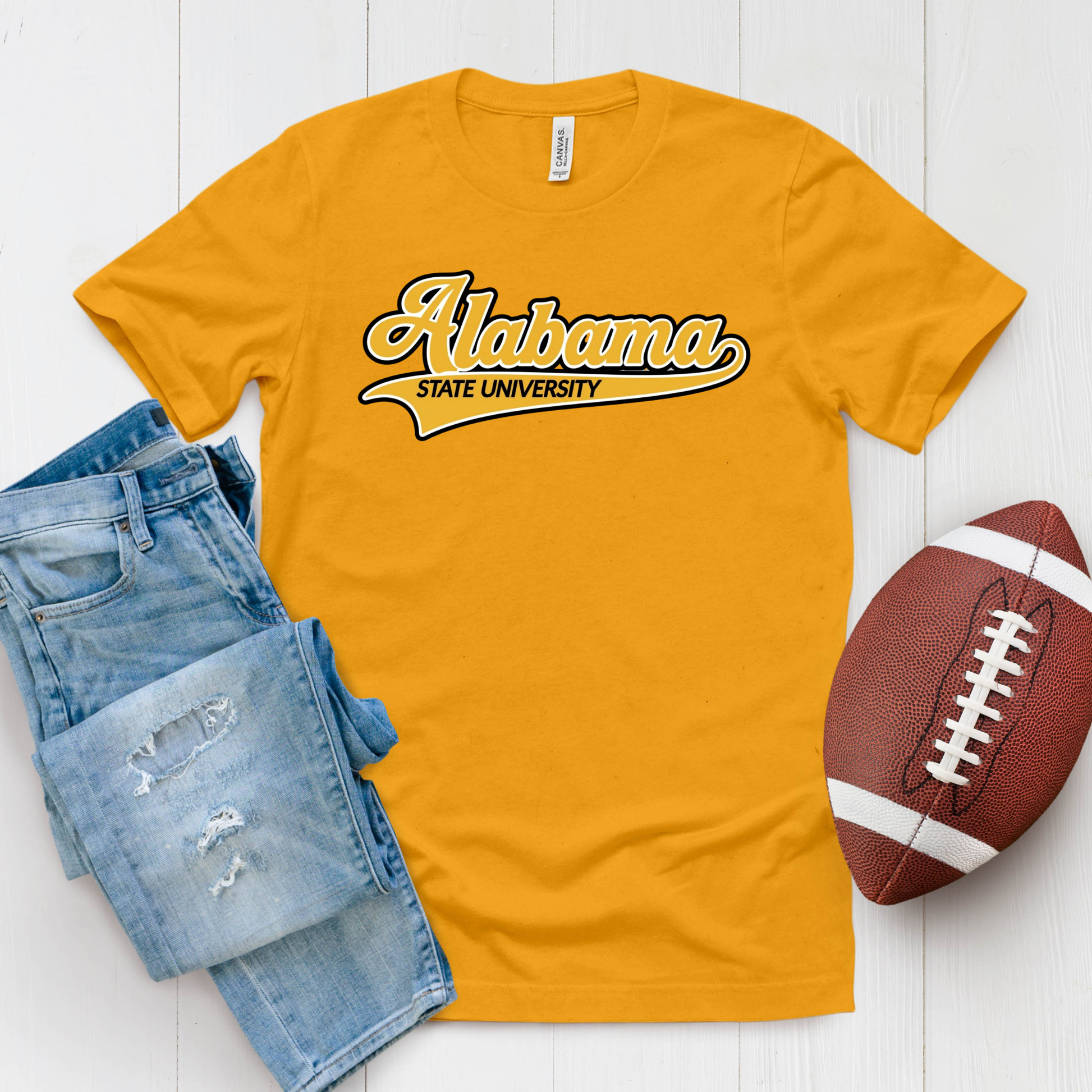 A gold crewneck t-shirt featuring a 'Hornets Nation' graphic with a hornet mascot, styled in a flat lay with blue jeans and a brown football on a white wood background.