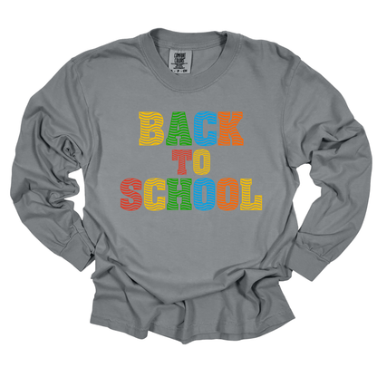A gray long-sleeve t-shirt with a colorful graphic text reading 'BACK TO SCHOOL' in wavy, striped letters of yellow, green, orange, and blue, displayed on a clean white background.