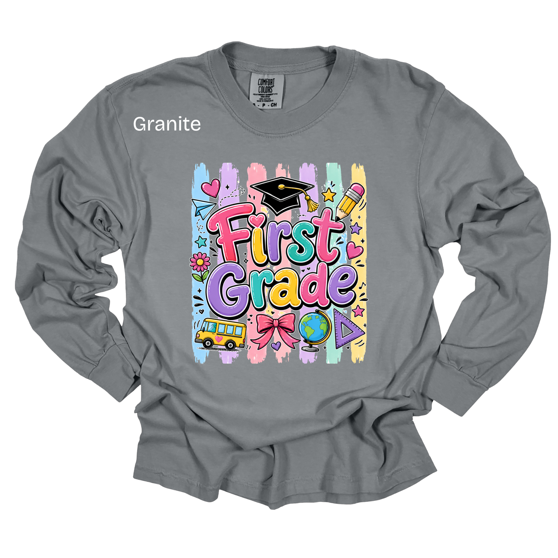 A gray long-sleeve t-shirt with a colorful 'First Grade' graphic on the front, featuring school-themed illustrations like a graduation cap, pencil, globe, and bus. The word 'Granite' is printed in white on the upper left chest.