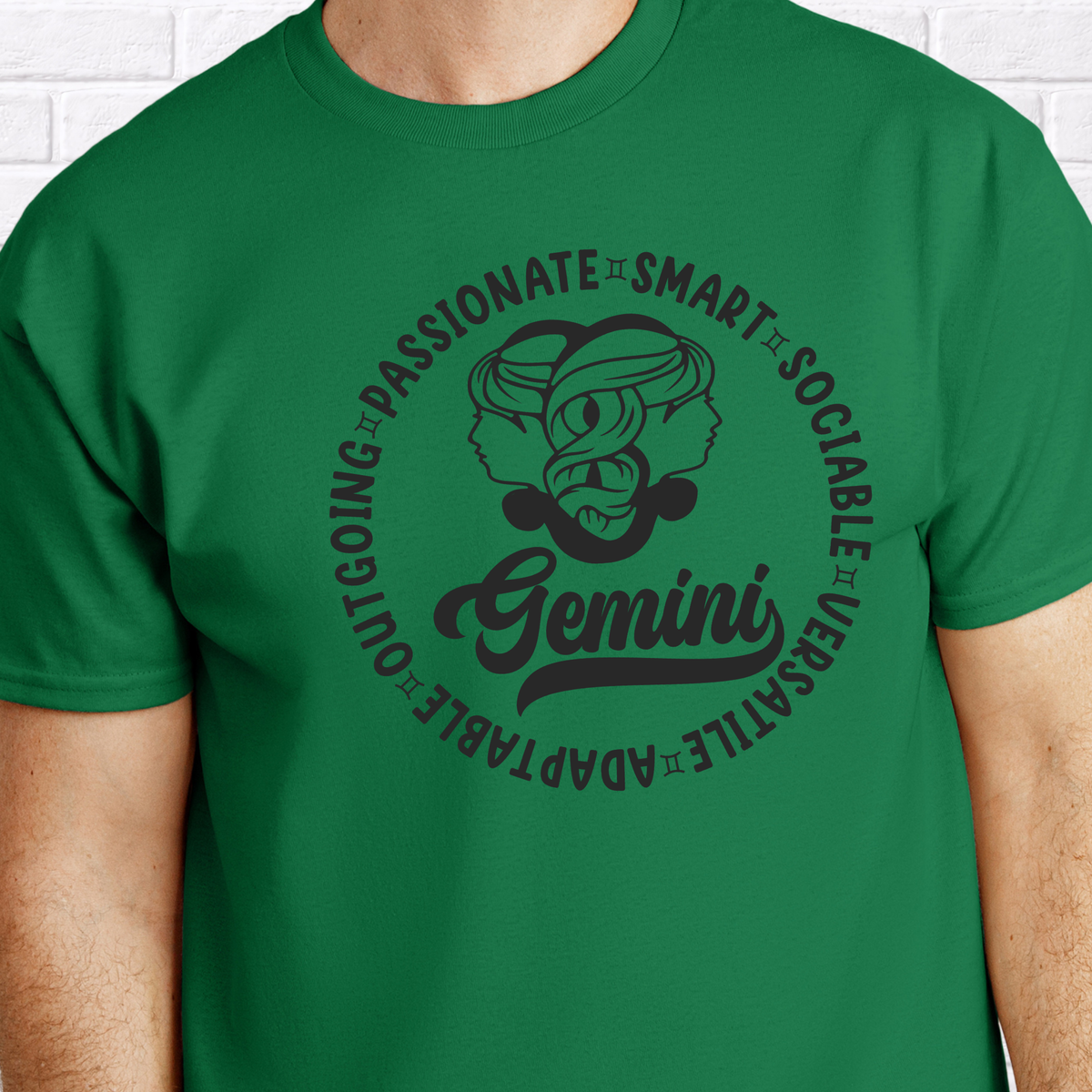 A green crewneck t-shirt featuring a black graphic print of a Gemini zodiac sign illustration and text, worn by a model against a white brick wall background.