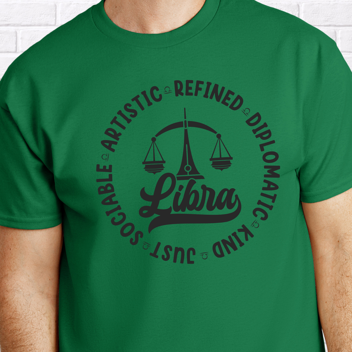 Woman wearing a white crewneck t-shirt featuring a black circular Libra zodiac graphic with a scales illustration, the word "Libra," and trait keywords like artistic, refined, diplomatic, kind, just, and sociable.