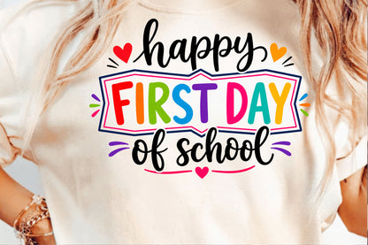 A close-up of a person wearing a cream-colored t-shirt with a colorful graphic that reads 'happy FIRST DAY of school' in black and rainbow-colored lettering.