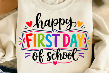A cream-colored sweatshirt featuring a colorful graphic that reads 'happy FIRST DAY of school' in black and rainbow-colored lettering, styled in a flat-lay arrangement.