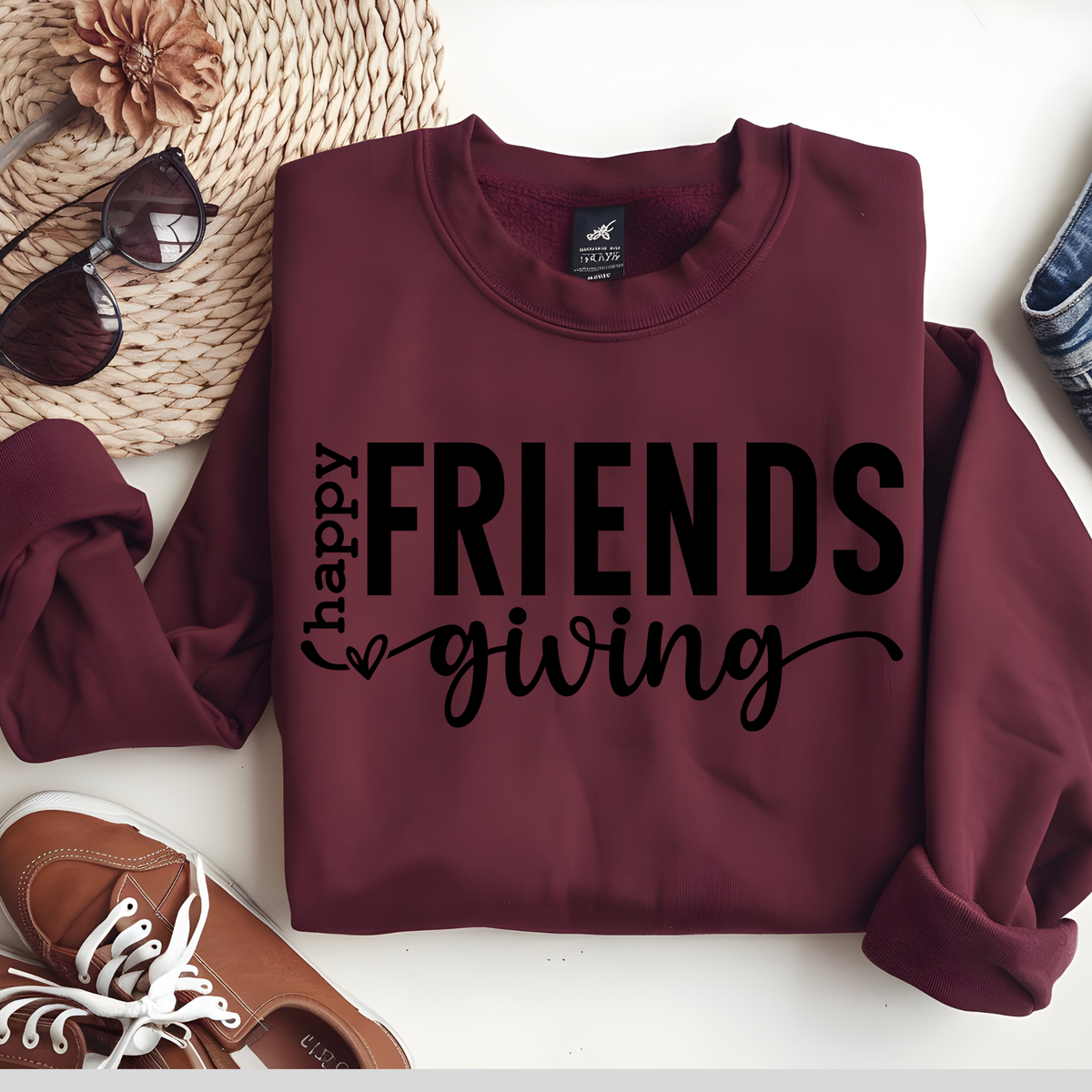 Maroon sweatshirt with 'happy friends giving' text on a white surface with accessories.