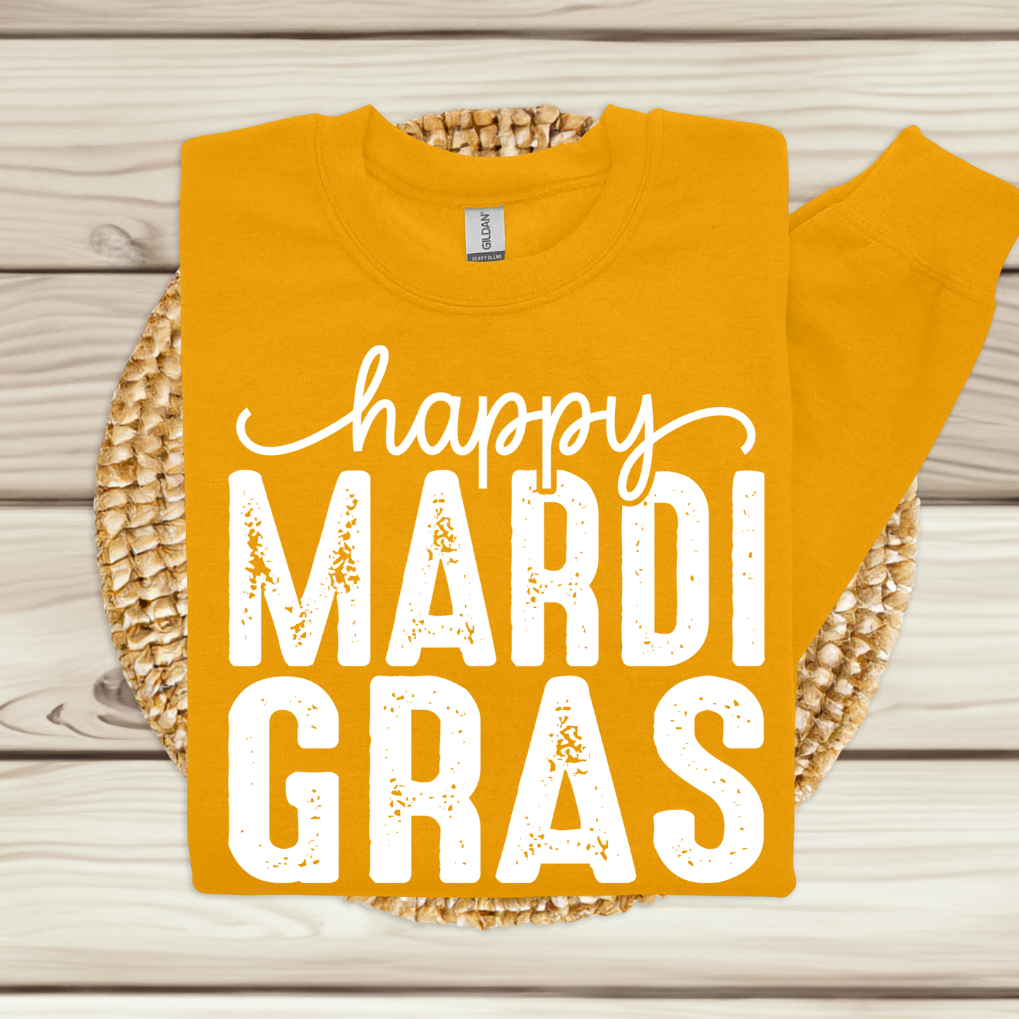 Yellow t-shirt with 'happy MARDI GRAS' text on a wooden surface