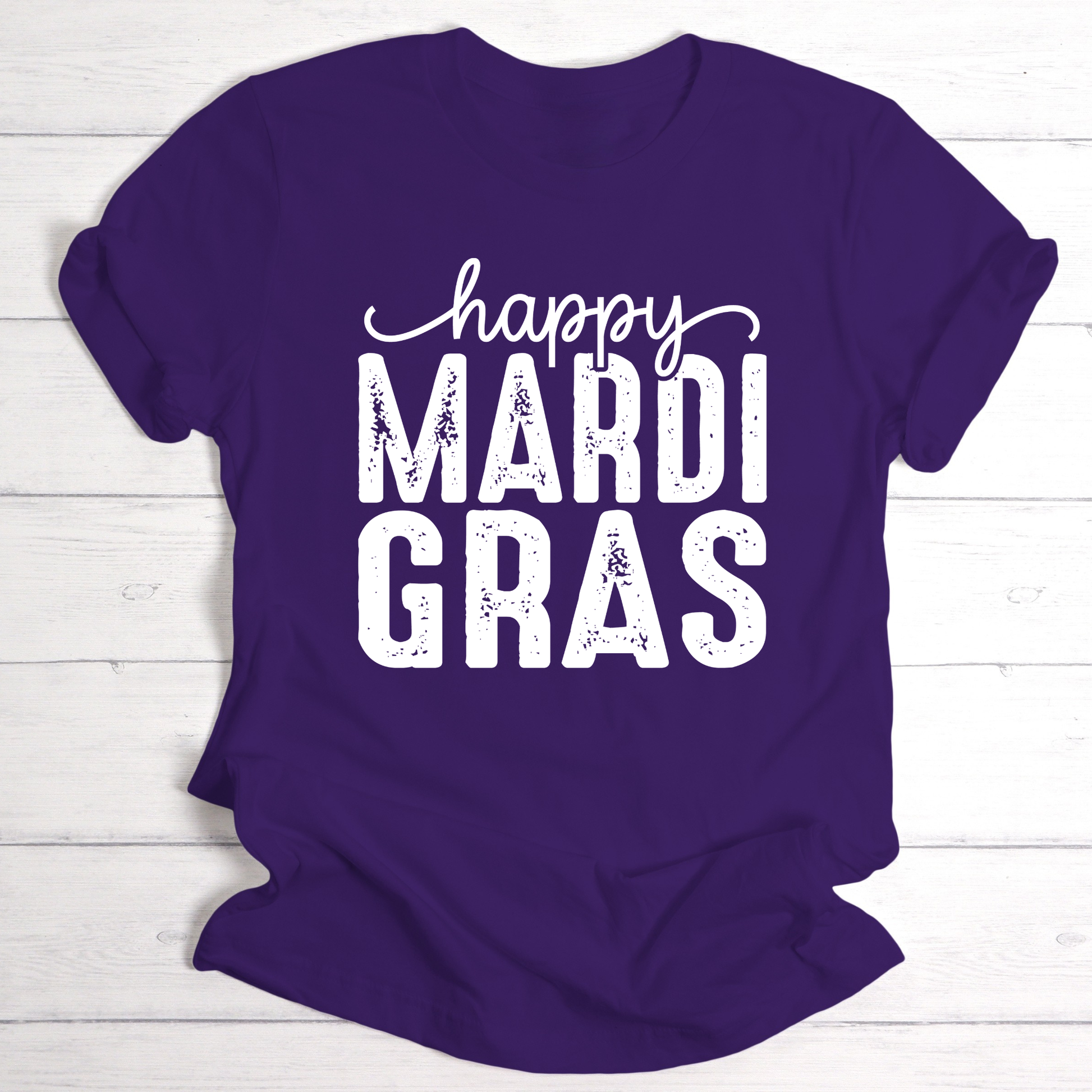 Purple t-shirt with 'happy MARDI GRAS' text on a white wooden background
