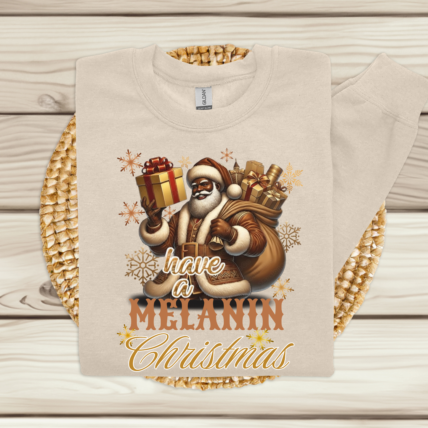 Beige sweatshirt with a graphic of Santa Claus holding gifts and text 'Have a Melanin Christmas' on a wooden surface.