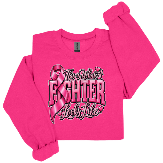 A bright pink long-sleeve sweatshirt with a graphic on the front that reads 'This is What A FIGHTER Looks Like' in stylized lettering with a pink ribbon and small hearts. The sweatshirt is laid flat on a white background with one sleeve rolled up.