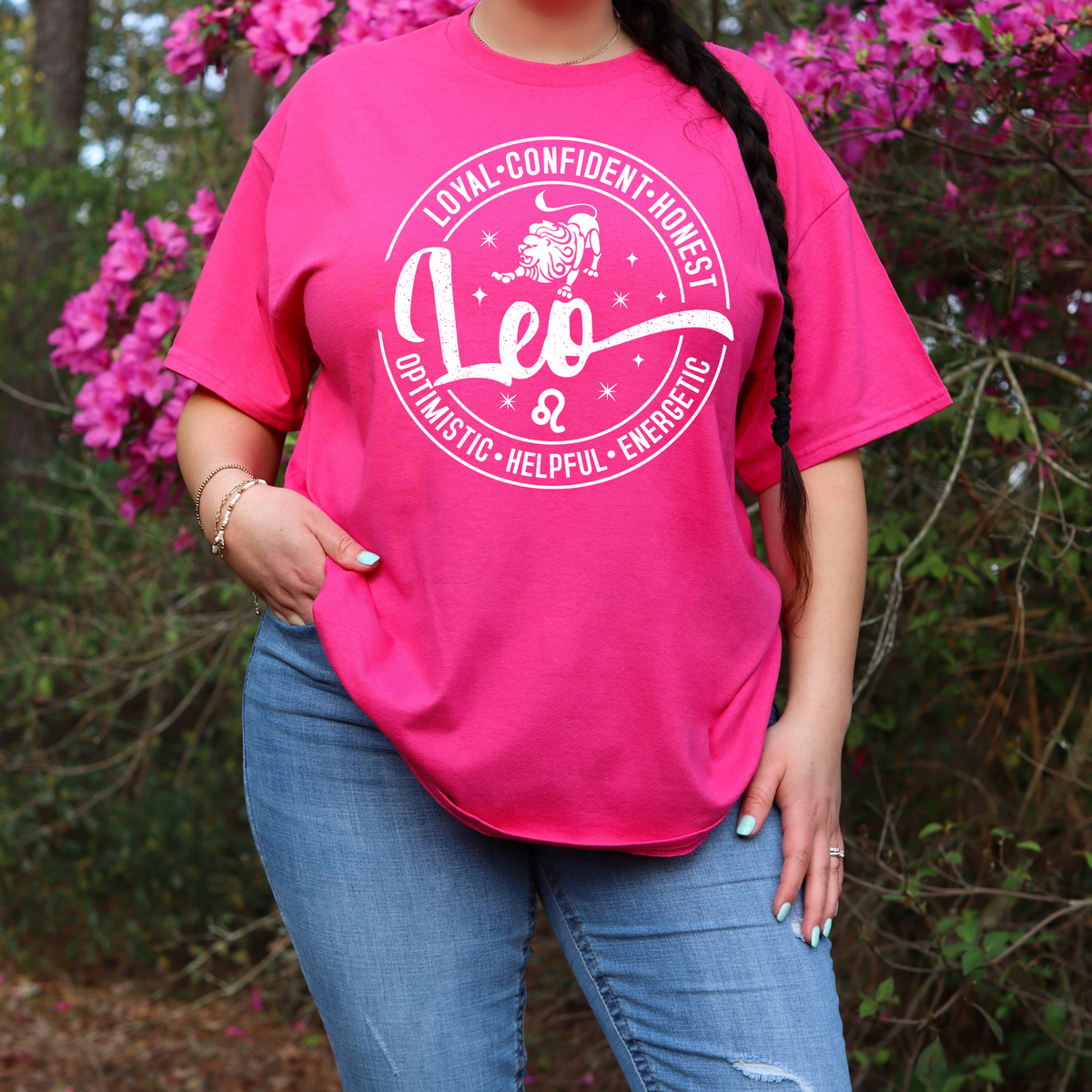 Woman wearing a vibrant pink Leo zodiac t-shirt featuring a white round graphic with a lion illustration, the word "Leo," and positive trait keywords like loyal, confident, honest, energetic, helpful, and optimistic.
