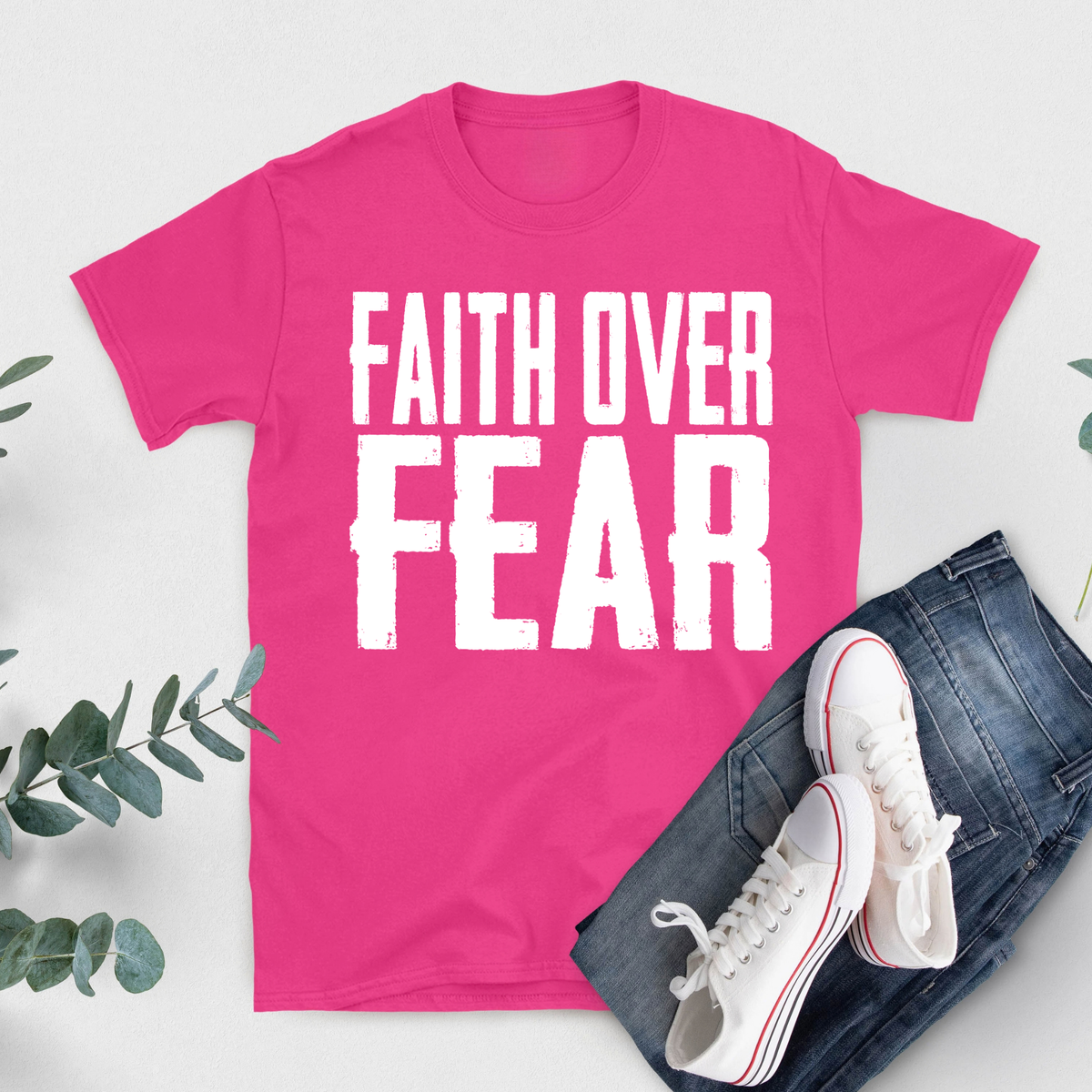 A bright pink short-sleeve T-shirt with bold white text reading 'FIGHT LIKE A QUEEN' laid flat on a light background, styled with blue jeans and white sneakers with red stripes.