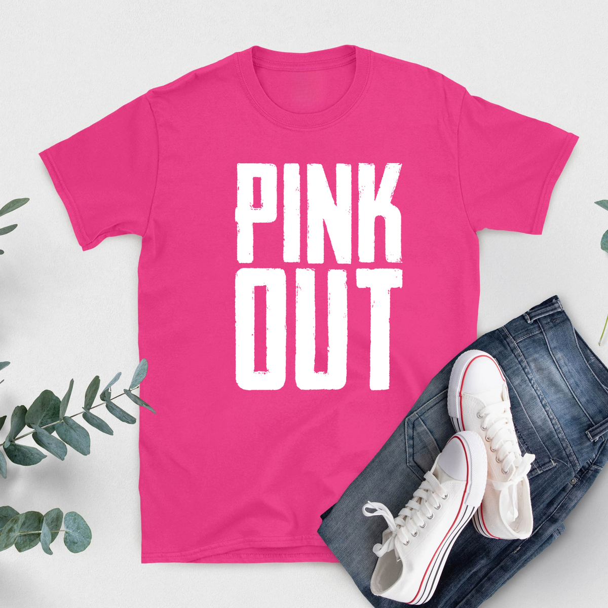 A bright pink short-sleeve T-shirt with bold white text reading 'FIGHT LIKE A QUEEN' laid flat on a light background, styled with blue jeans and white sneakers with red stripes.