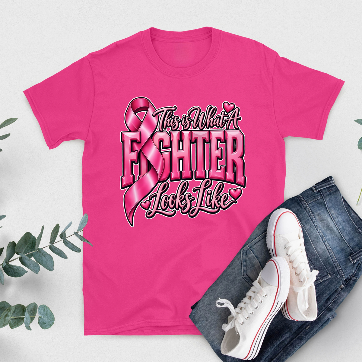 A bright pink short-sleeve T-shirt with bold white text reading 'FIGHT LIKE A QUEEN' laid flat on a light background, styled with blue jeans and white sneakers.