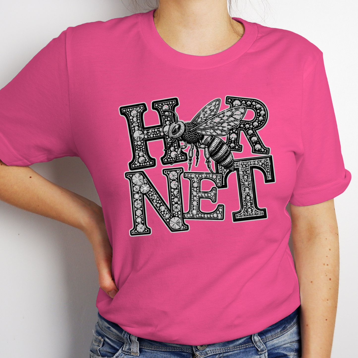 A woman wearing a bright pink short-sleeve t-shirt with a black and white graphic that reads 'EAGLES' in a textured, gemstone-like font, featuring an eagle head design. The model is also wearing blue jeans.