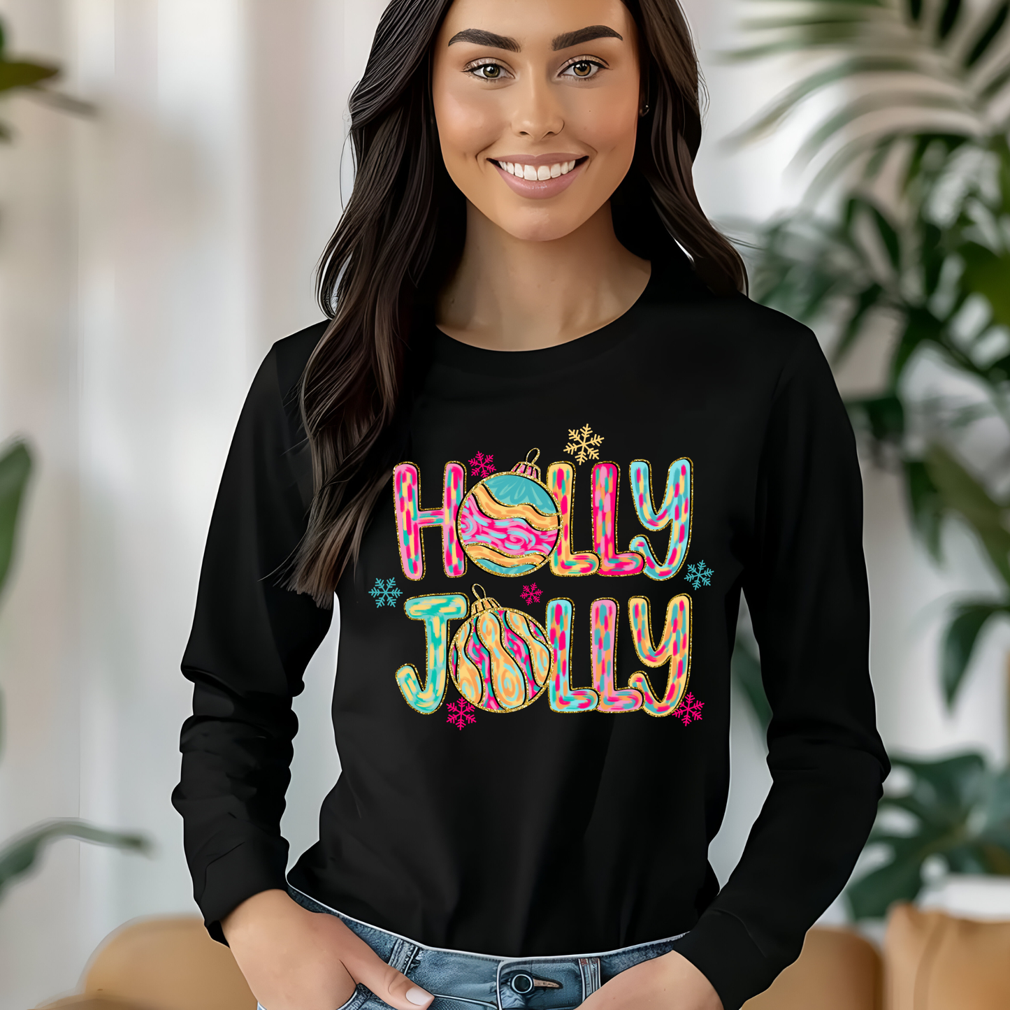 Woman wearing a black long-sleeve shirt with 'Holly Jolly' design, sitting indoors with plants in the background.