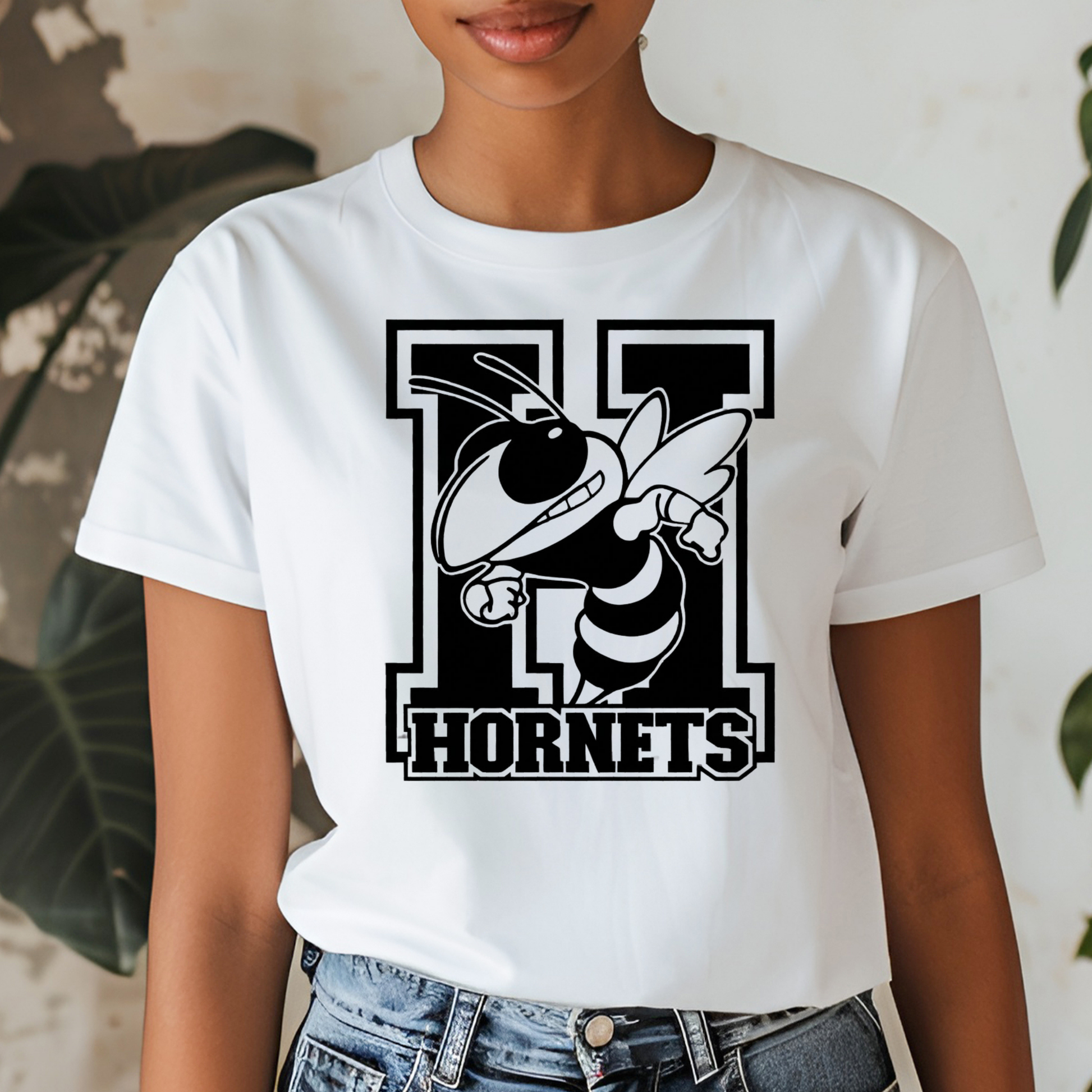 A woman wearing a white short-sleeve t-shirt with a black and white graphic of a hornet mascot and the word 'HORNETS' on the front, paired with blue jeans.
