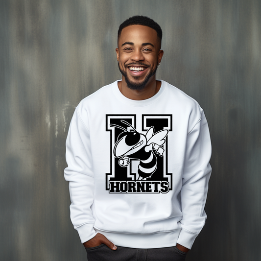 A smiling man wearing a white crewneck sweatshirt with a black and white hornet graphic and the word 'HORNETS' on the front, posed against a textured gray studio background.