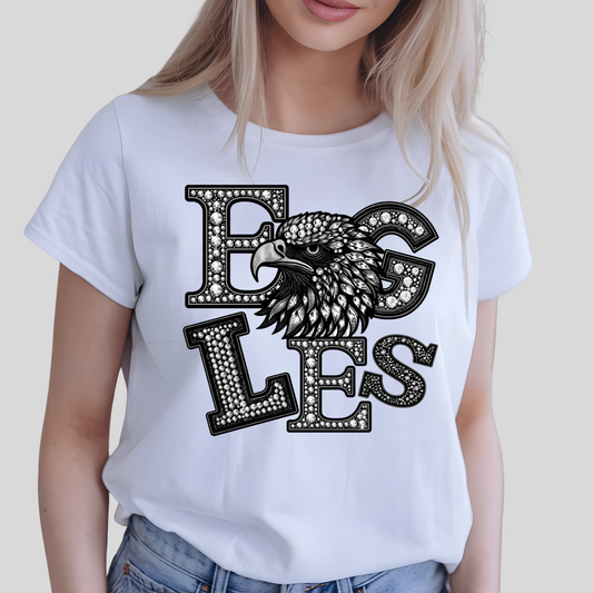 A woman wearing a white short-sleeve t-shirt with a black and white graphic of an eagle's head integrated into the letters 'EGLES'.