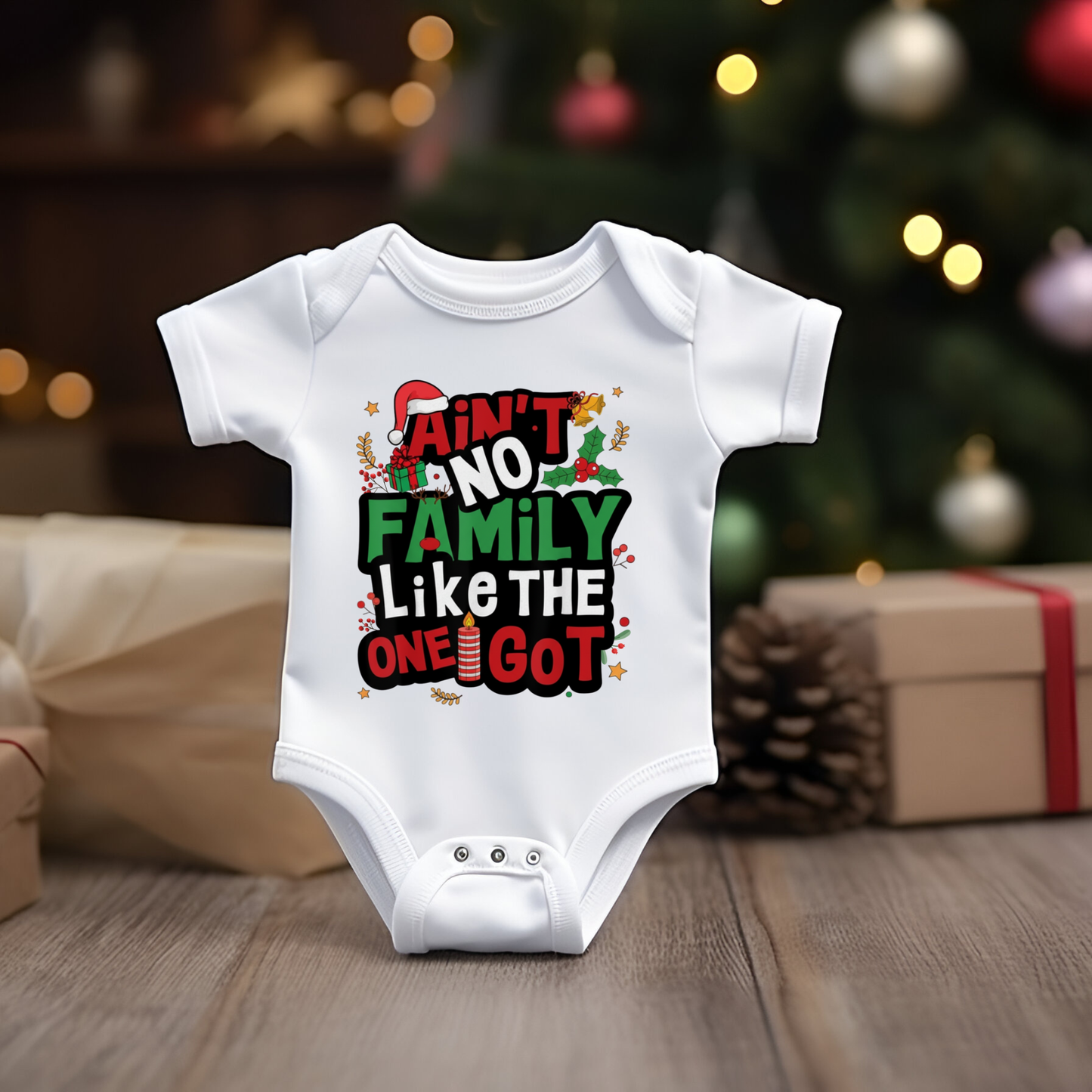 White baby onesie with Christmas-themed text in front of a decorated Christmas tree.