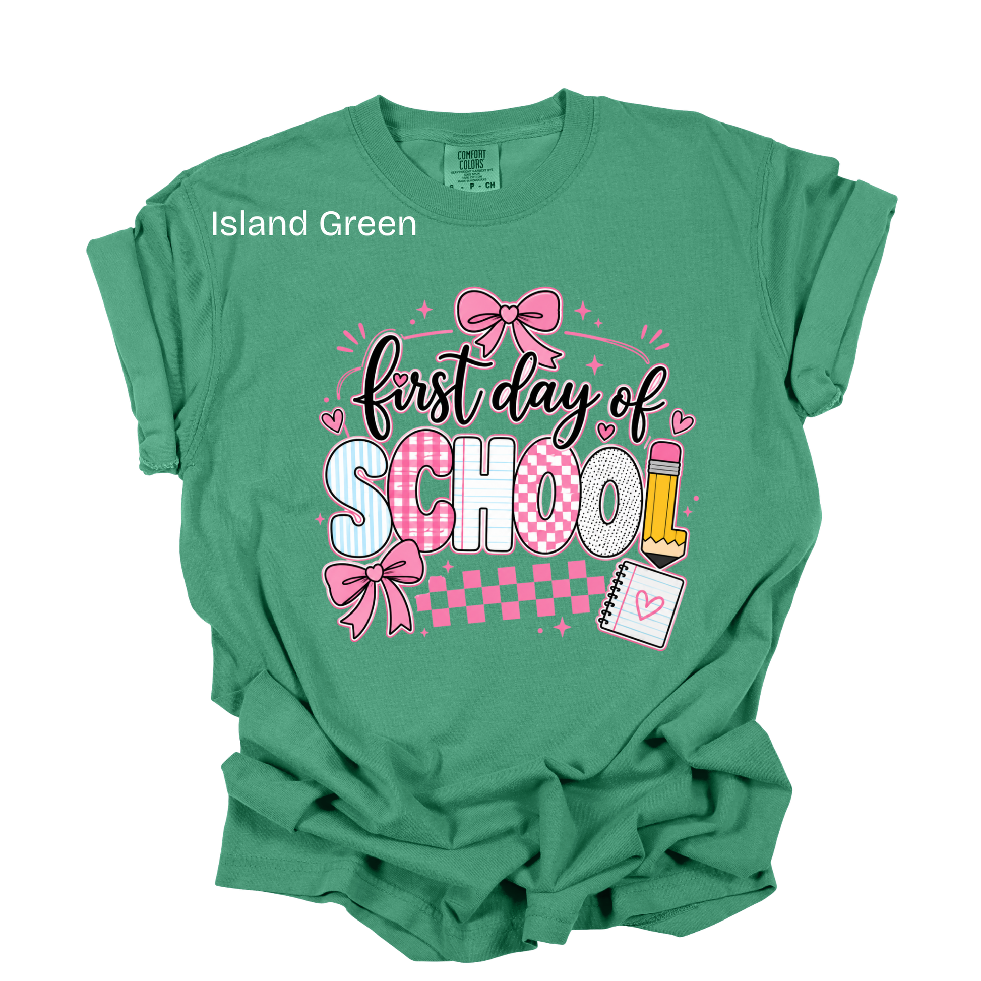 A green short-sleeve t-shirt with a 'first day of SCHOOL' graphic on the front, featuring pink bows, checkered patterns, and school-themed illustrations, shown on a plain white background.