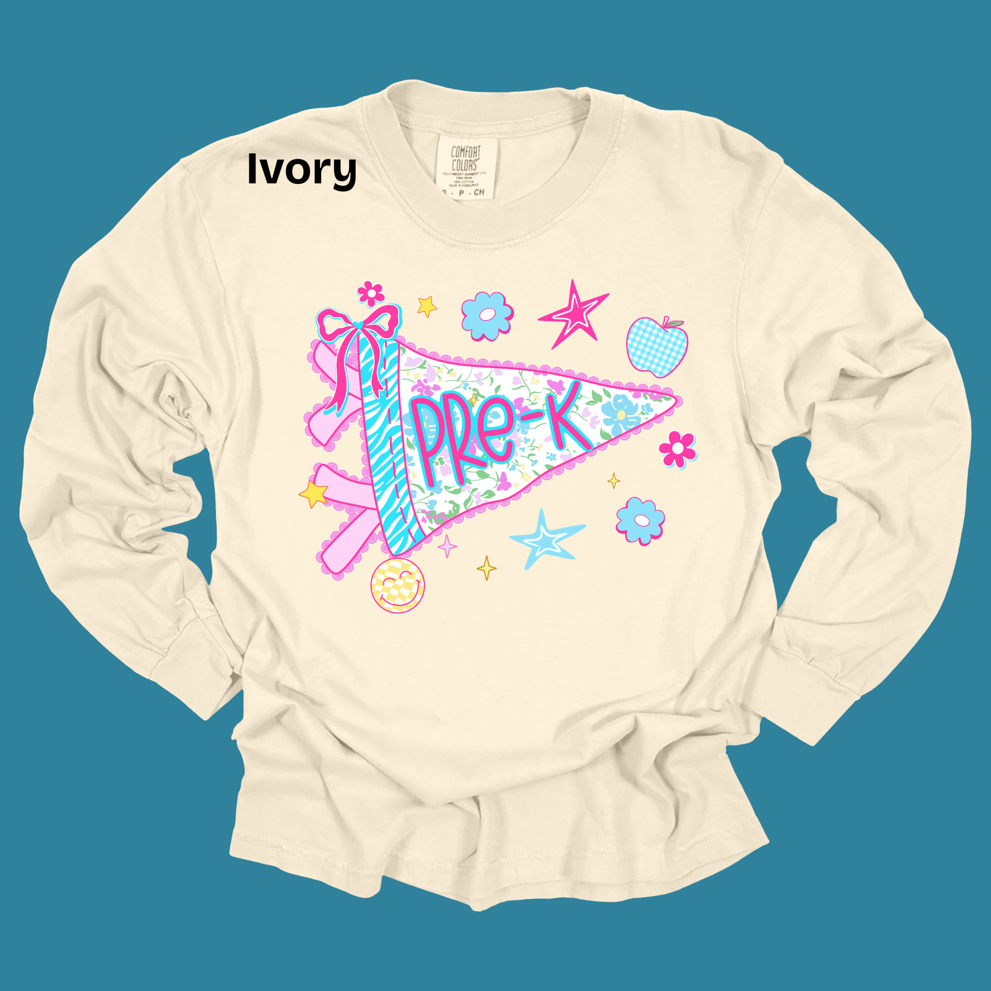 An ivory long-sleeve t-shirt with a colorful 'PRE-K' pennant graphic, displayed flat against a solid teal background. The word 'Ivory' is printed in black near the collar, and the inner neck label shows the brand 'Canvas'.