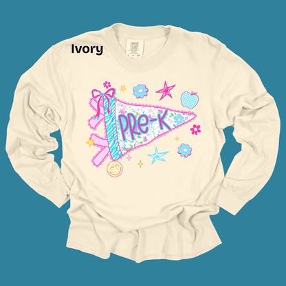 An ivory long-sleeve t-shirt with a colorful 'PRE-K' pennant graphic, displayed flat against a solid teal background. The word 'Ivory' is printed in black near the collar, and the inner neck label shows the brand 'Canvas'.
