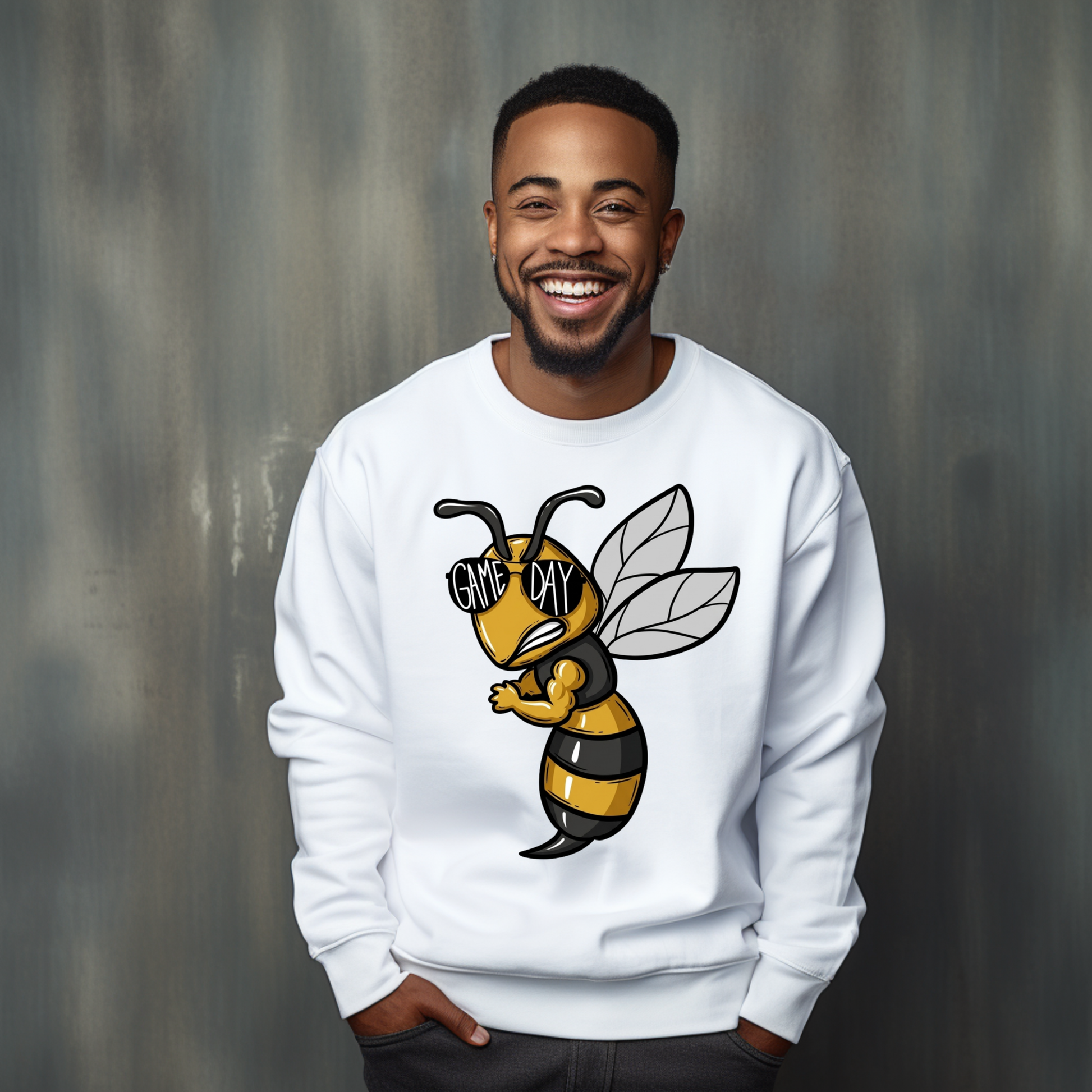 A smiling man wearing a white crewneck sweatshirt with a cartoon bee graphic on the front. The bee is yellow and black striped with the text 'GIVE MY' on its wing, set against a textured gray studio background.
