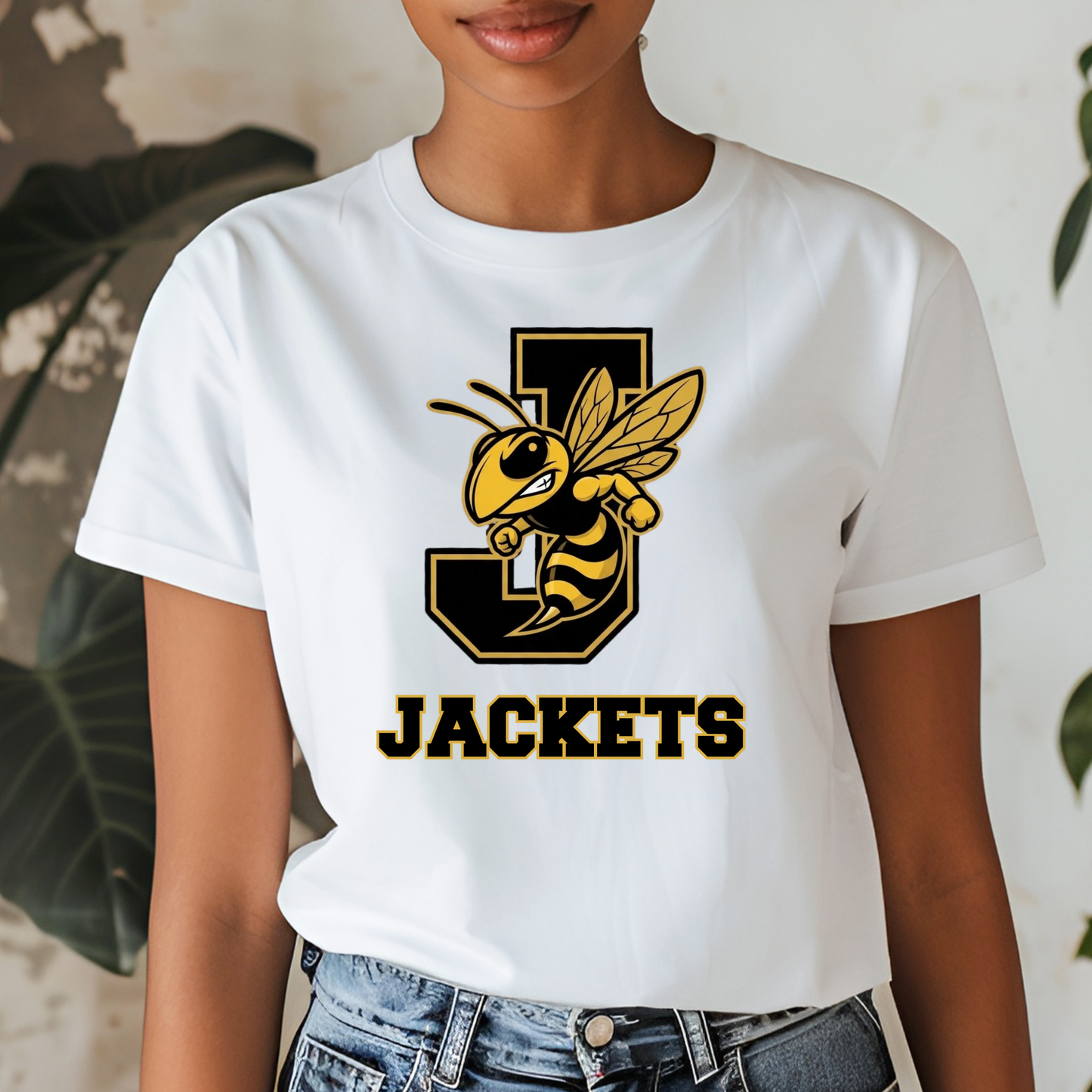 A woman wearing a white short-sleeve graphic T-shirt with a large yellow and black bee mascot and the word 'JACKETS' on the front, paired with blue jeans.