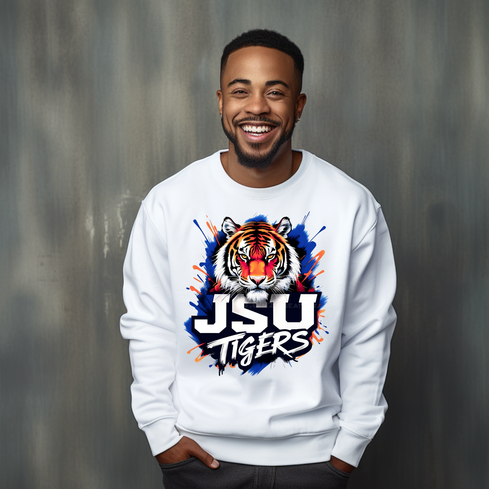 A smiling man wearing a white crewneck sweatshirt with a colorful JSU Tigers tiger graphic on the front, standing against a textured gray studio background.