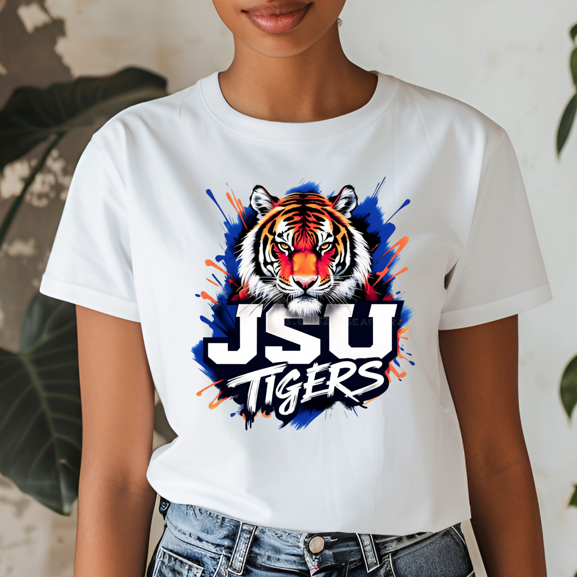 A woman wearing a white short-sleeve t-shirt with a colorful graphic of a tiger's face and the text 'JSU TIGERS' in white, blue, and orange paint splatter.