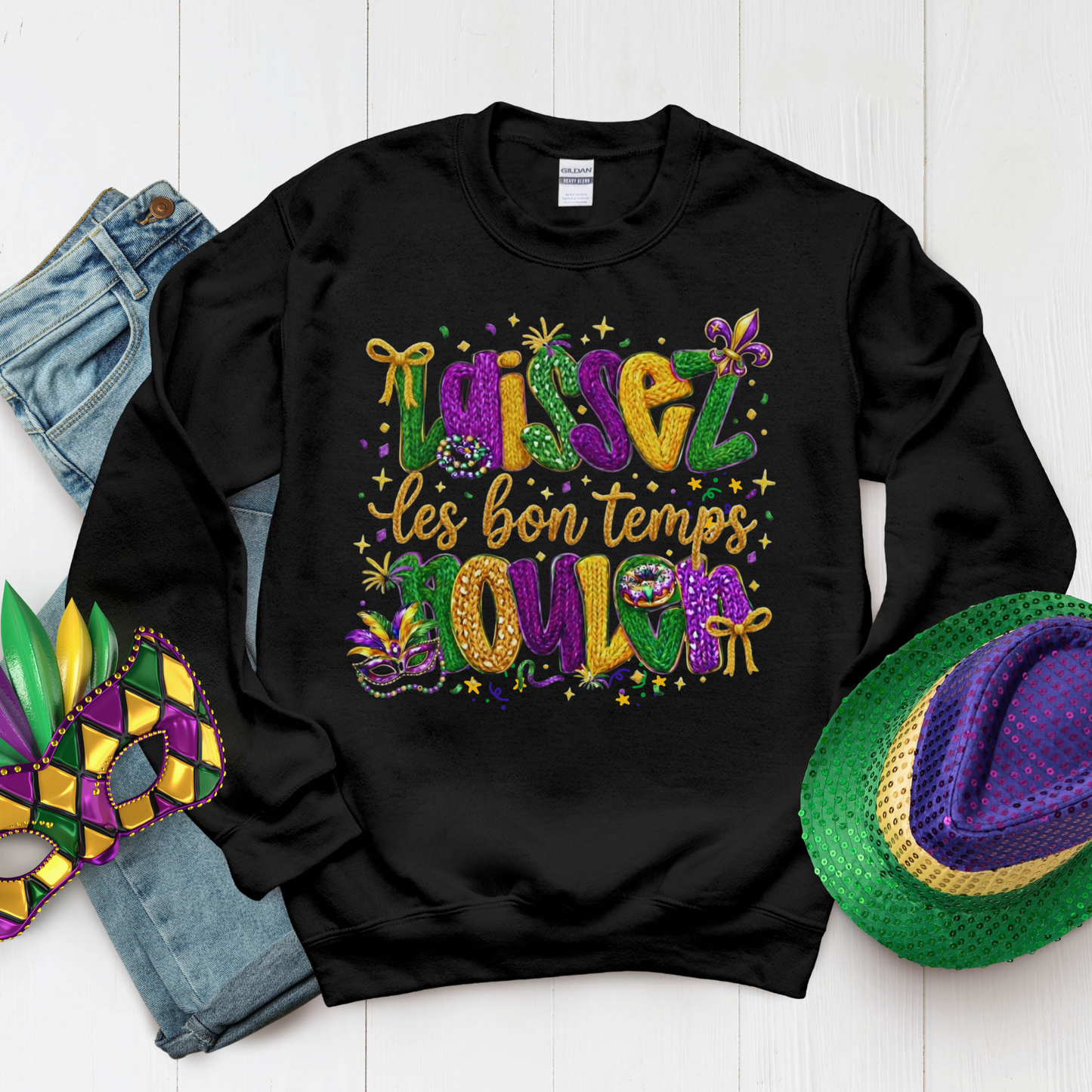 Black sweatshirt with colorful Mardi Gras text, surrounded by Mardi Gras accessories on a white background.