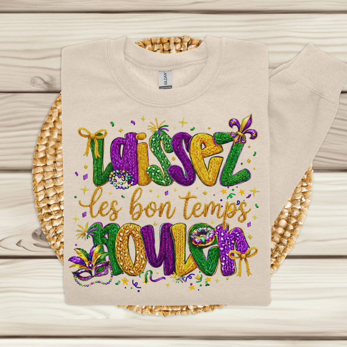 Beige t-shirt with colorful Mardi Gras-themed text and beads on a wooden surface